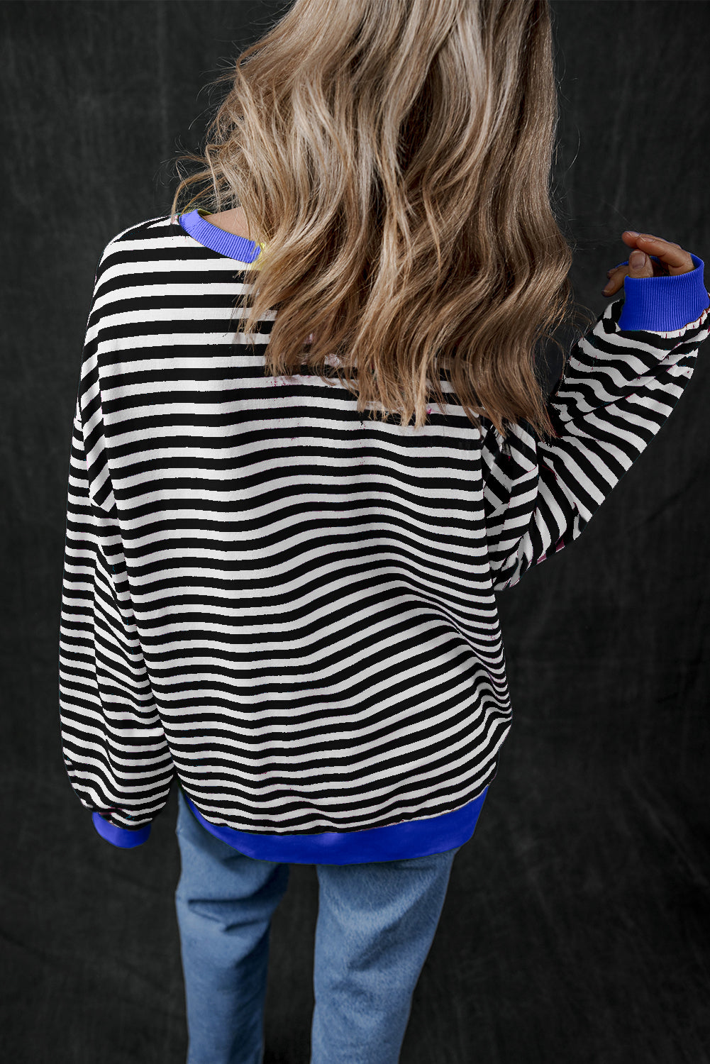 Standing with their back to the camera, a person with long, wavy hair wears the Black Stripe Oversized Contrast Trim Pullover Sweatshirt paired with matching blue pants.