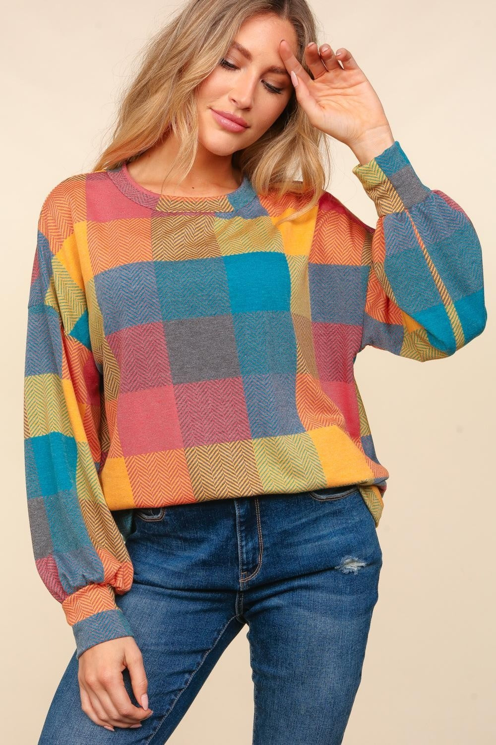 A woman wearing a stylish Haptics Round Neck Color Block Plaid Top and blue jeans poses against a beige background.