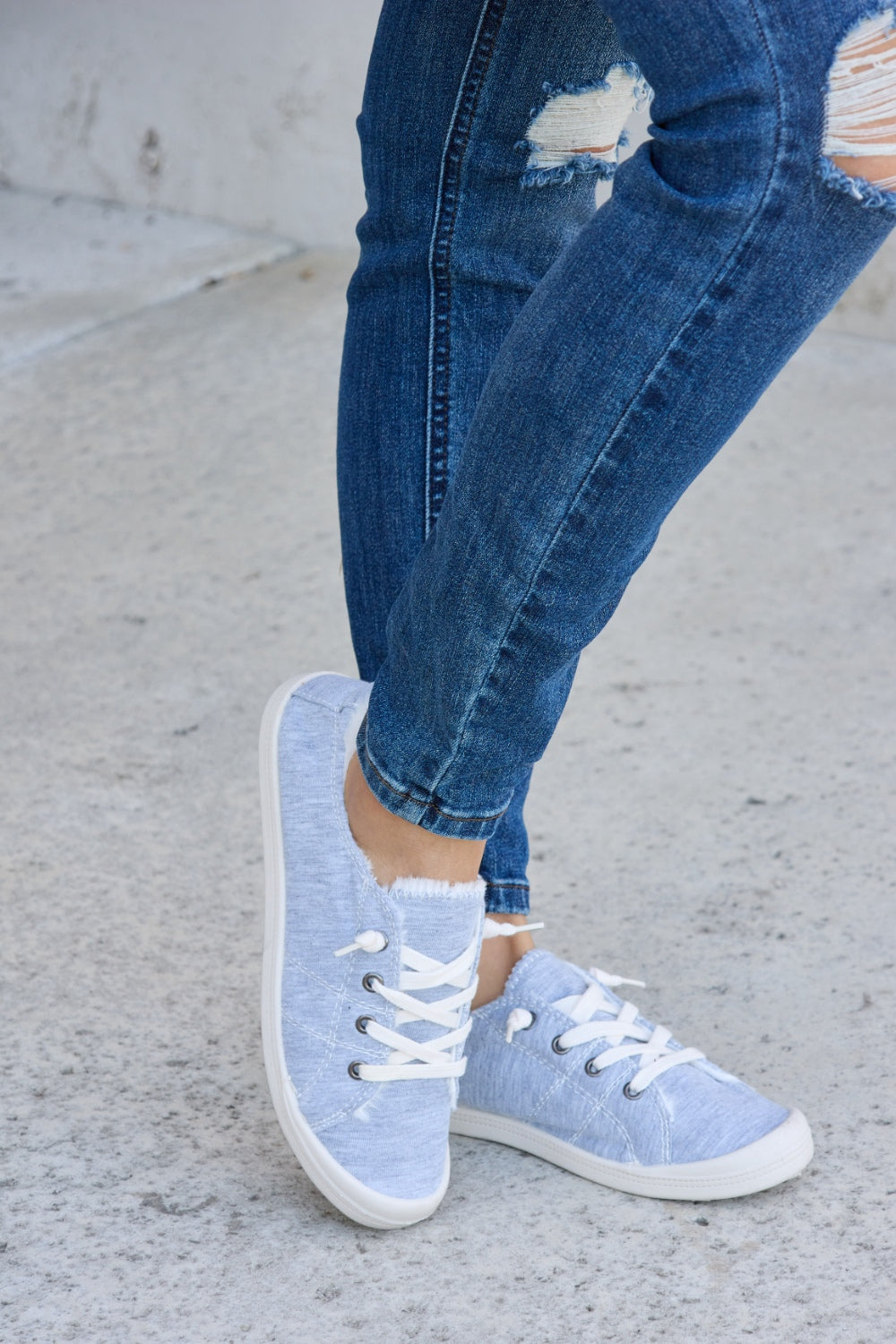 Person wearing ripped blue jeans and Forever Link Lace-Up Plush Thermal Flat Sneakers in grey with white laces, standing on a concrete surface.