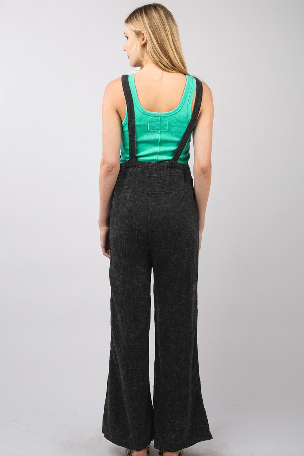 A person wearing the VERY J Texture Washed Wide Leg Overalls and a green top stands against a gray background, paired with sandals, presenting a stylish and relaxed look.