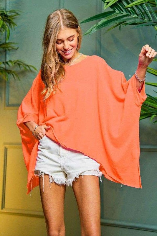 A woman wearing a Solid Round Neck Loose Fit Kimono Sleeve Sweater in orange and white shorts stands indoors near green plants.