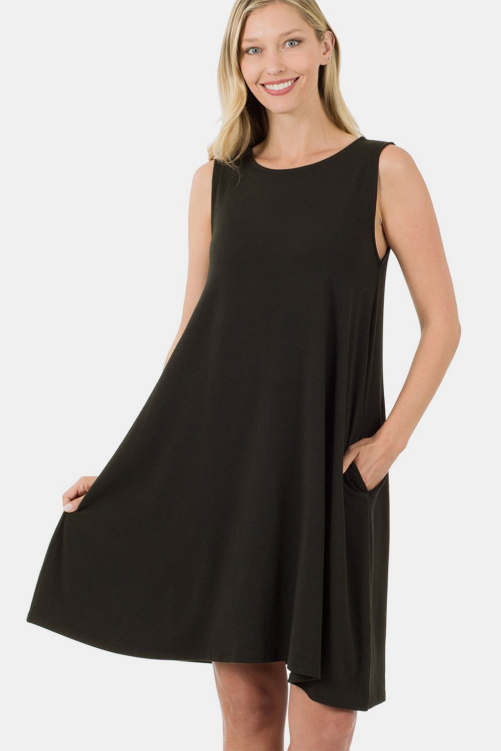 A woman with blonde hair smiles while wearing the Zenana Full Size Sleeveless Flared Dress with Side Pockets in black. She holds one side of the dress with her hand and has her other hand in the pocket, showcasing this versatile wardrobe piece.