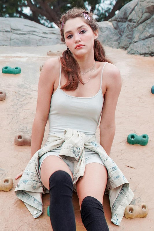 The Loving Me Fitted Sleeveless Romper, featuring a fitted bodice and spaghetti straps in black, hangs gracefully on a wooden hanger against a white wall.