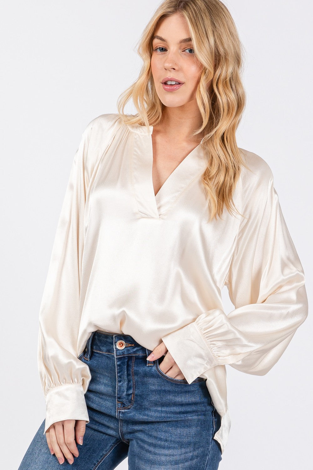 A person is wearing a SAGE + FIG Notched Long Sleeve Blouse in cream-colored satin paired with blue jeans.