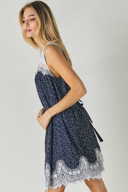 A woman wearing the Printed Sleeveless Lace Trim Mini Dress is seated against a light background.