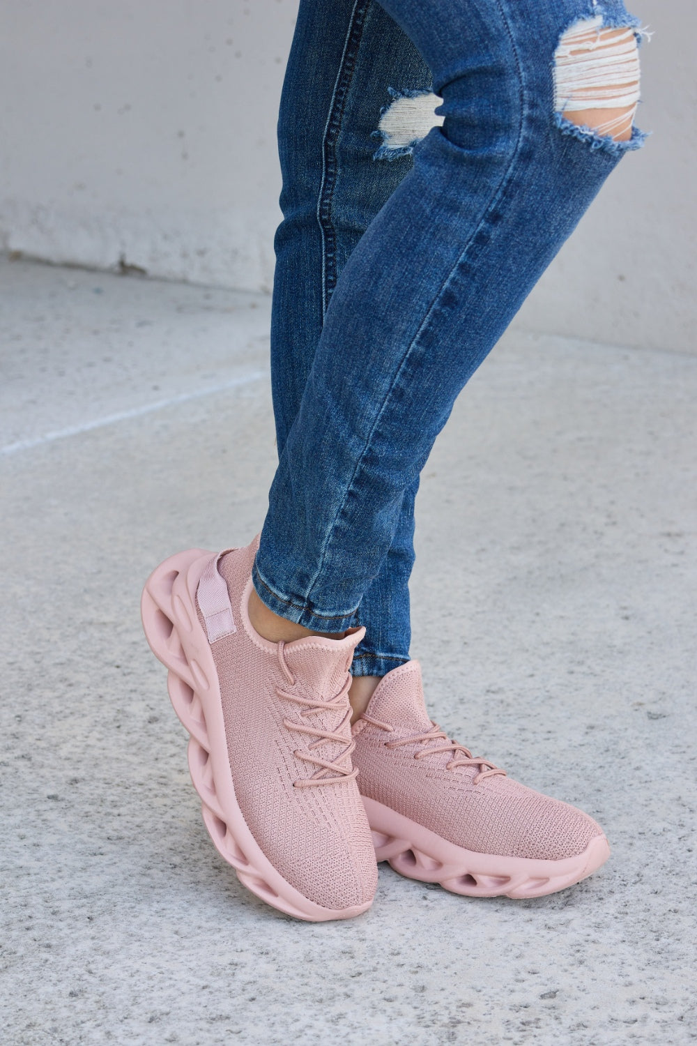 Person wearing blue ripped jeans and Forever Link Mesh Breathable Platform Athletic Shoes in light pink, standing on a concrete surface.