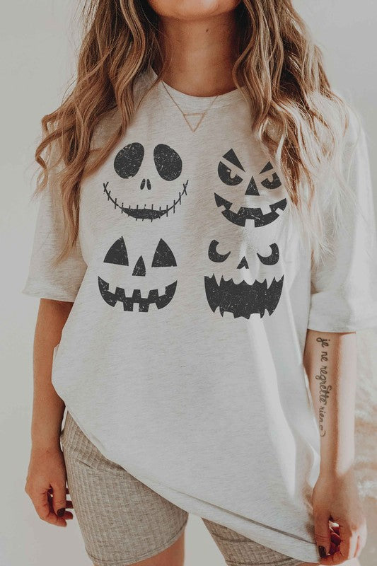 A person wears the SCARY PUMPKINS Graphic Tee, featuring four black, scary pumpkin faces, paired with checkered shorts.