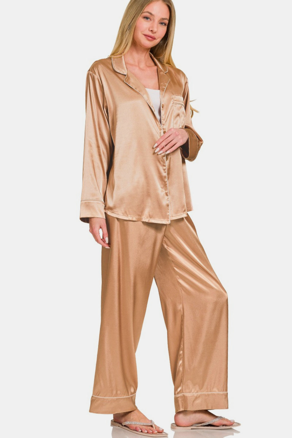 The woman stands elegantly in the Zenana Satin Long Sleeve Shirt and Pants Pajama Set, her hand resting on the collar of the shirt, complementing the ensemble’s elastic waist pants.