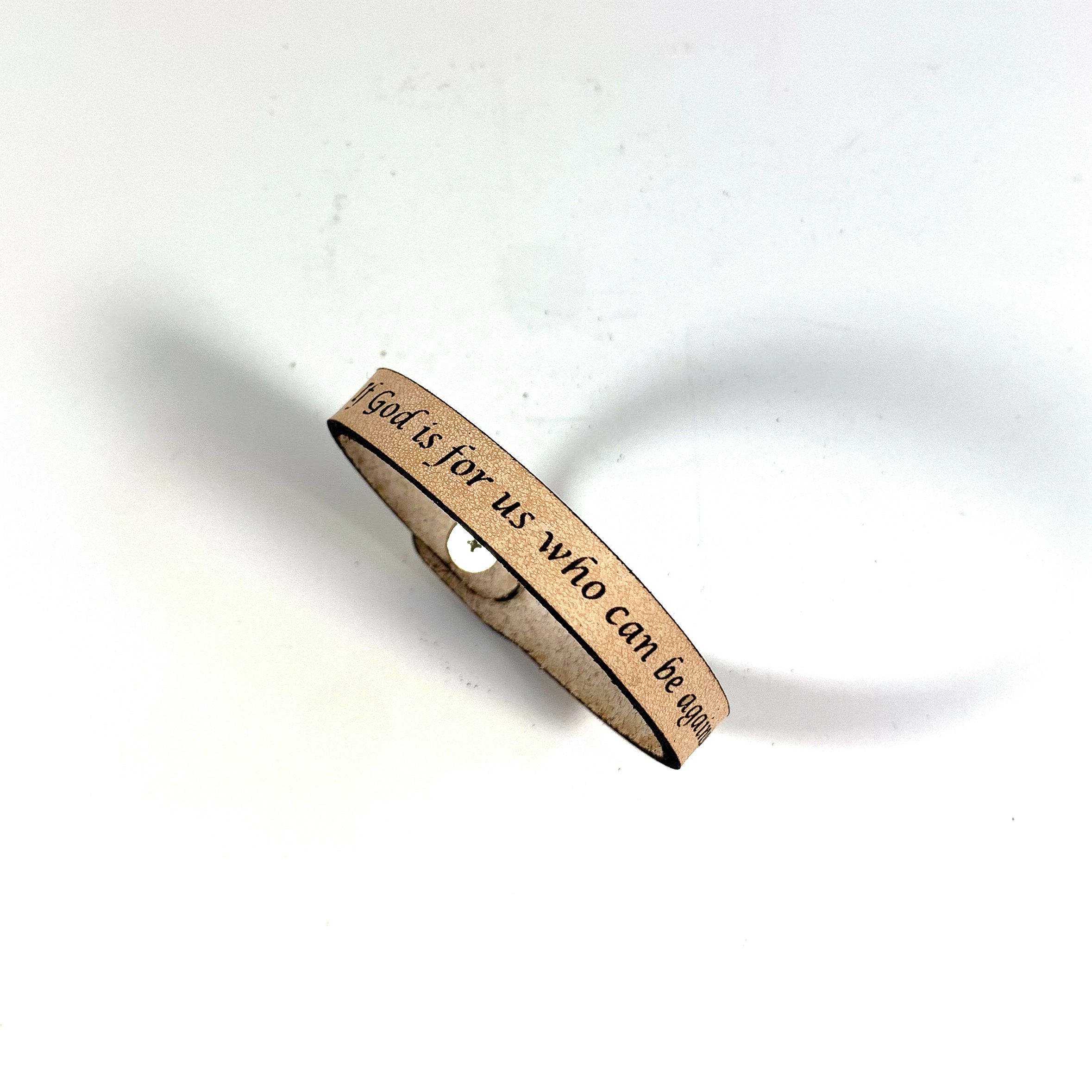 The Spiritual Quote Bracelet made of genuine leather features an adjustable button closure and is inscribed with the message: "If God is for us, who can be against us.