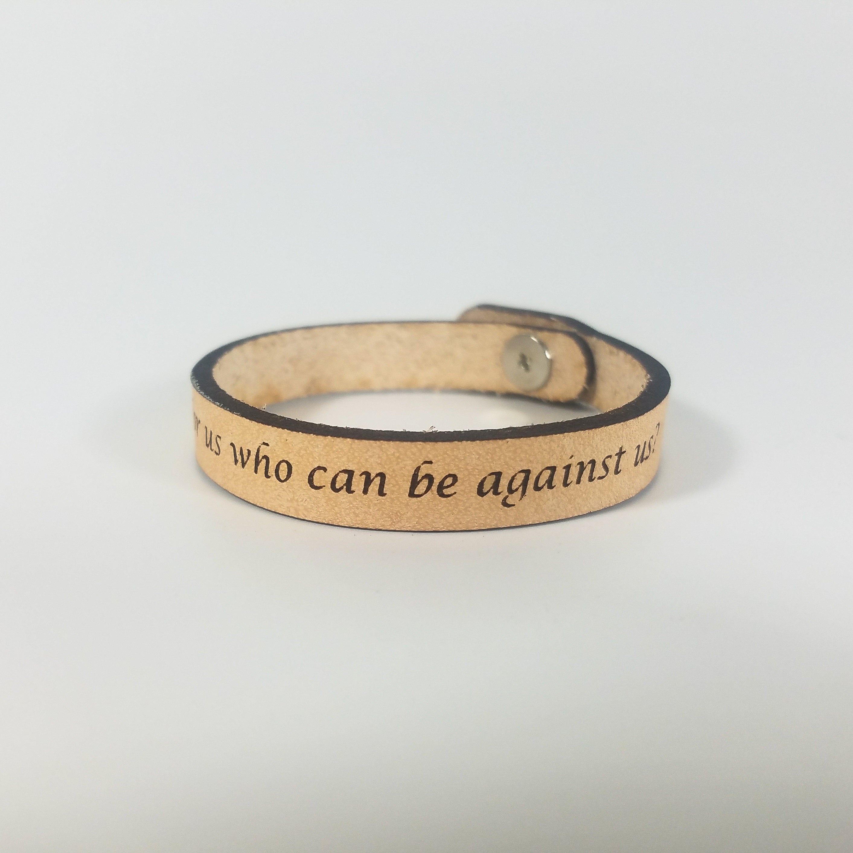 The Spiritual Quote Bracelet made of genuine leather features an adjustable button closure and is inscribed with the message: "If God is for us, who can be against us.