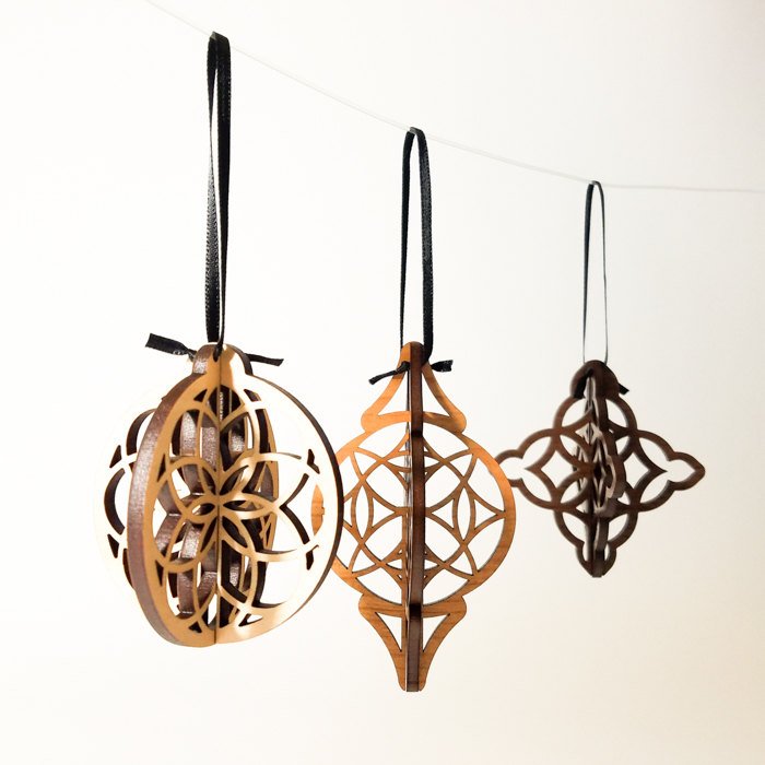 Three intricately carved Wood Christmas Ornaments hang from black ribbons against a white background, showcasing a modern ornament design.