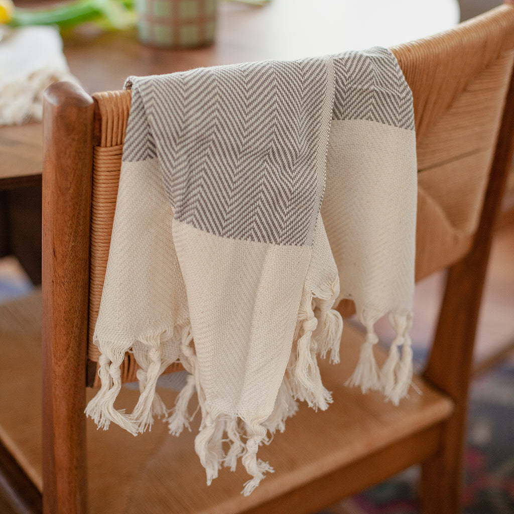 Product: The Herringbone Turkish Hand Towel is crafted from 100% Turkish cotton and displays a blue and white herringbone design, accented with a cream fringe border.