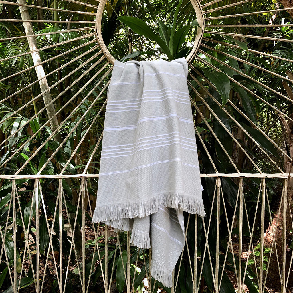 The Classic Terry Turkish Towel is a handmade white towel featuring horizontal gray stripes and fringed edges, ideal for enhancing the elegance of your bath collection.