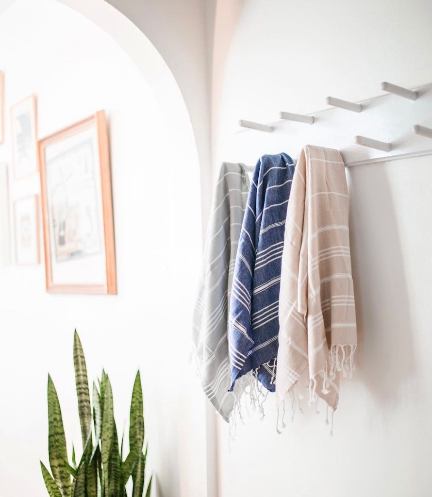 The Classic Turkish Hand Towels in five elegant striped designs, featuring shades of blue, brown, beige, navy, and grey, are beautifully displayed. Made from 100% Turkish cotton and adorned with white fringe on one end, they offer exceptional absorbency for all your needs.