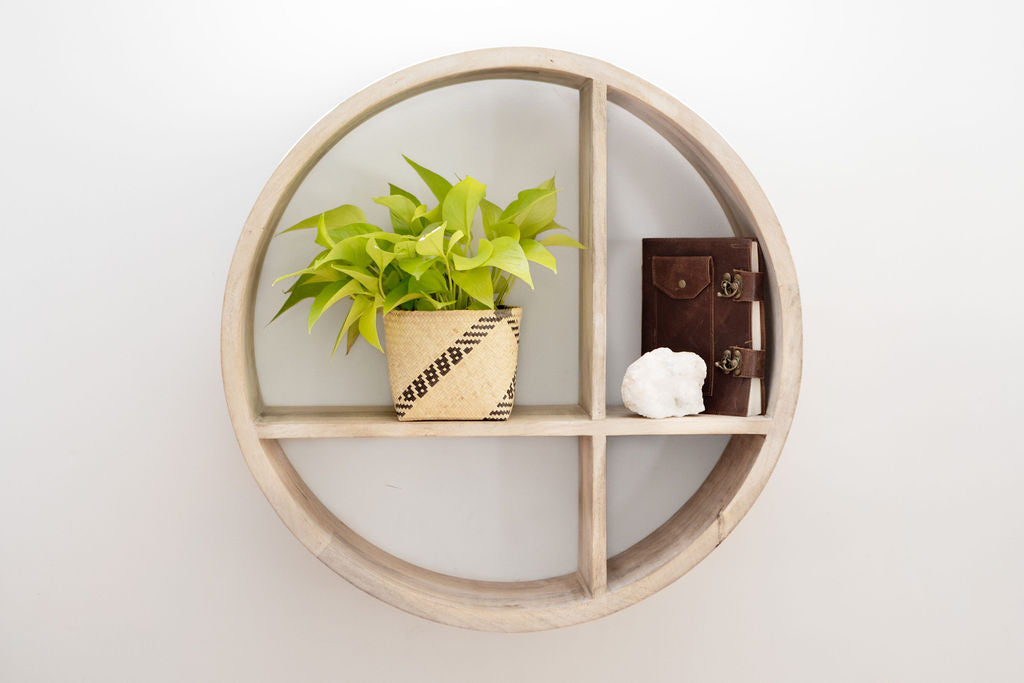 Round wooden wall shelf with four sections, showcasing a 6" Neon Pothos in a planter basket, a closed leather journal, and a white stone.