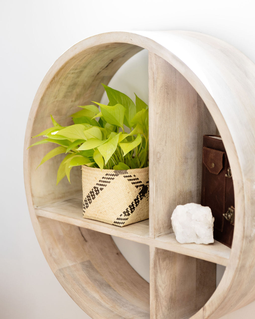 Round wooden wall shelf with four sections, showcasing a 6" Neon Pothos in a planter basket, a closed leather journal, and a white stone.