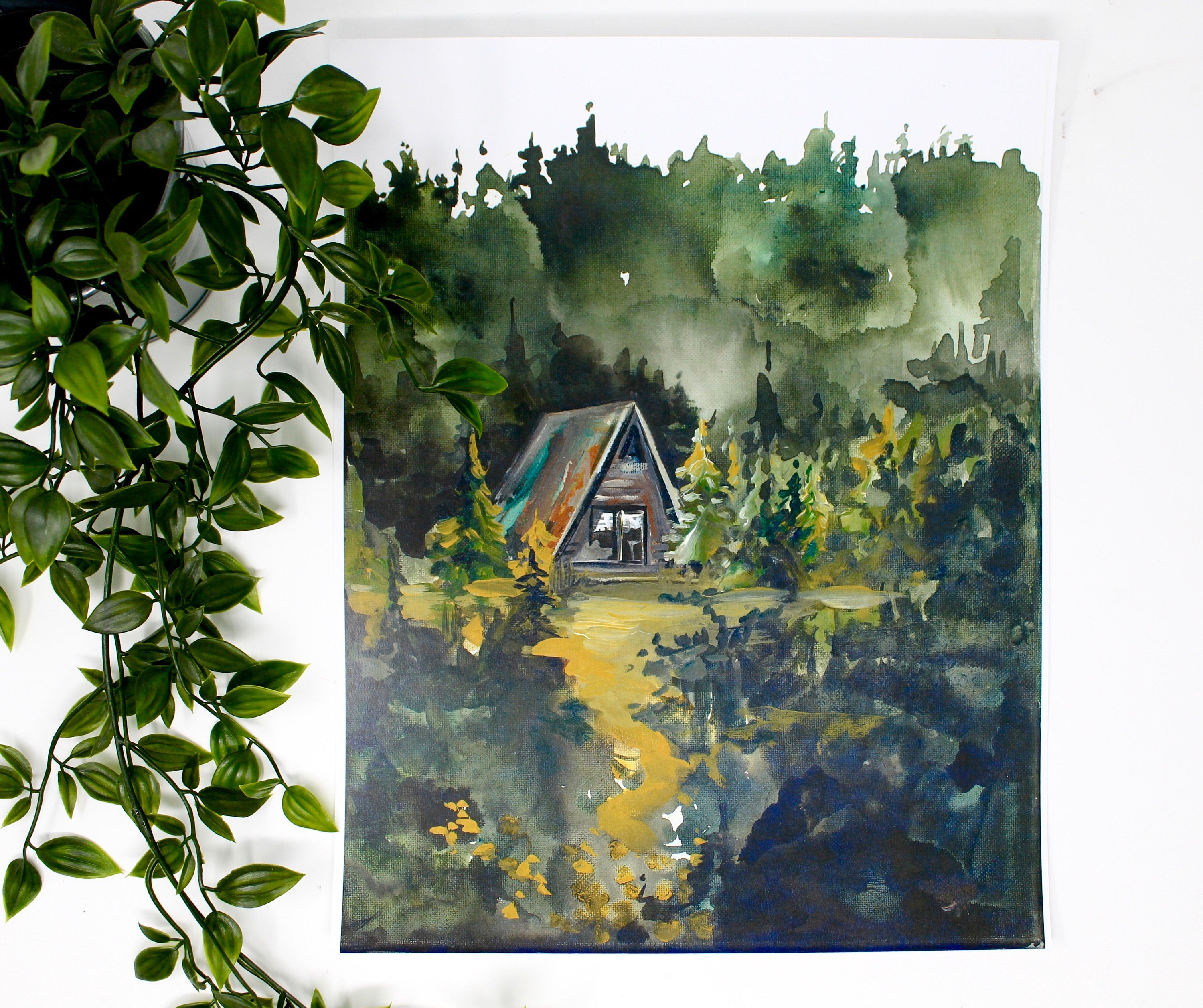 The Cozy Cabin Print 11x14 Adventure Print captures the allure of a watercolor painting portraying a cabin nestled in a dense, dark forest with an inviting path. This piece of home decor is perfect for adventure lovers and inspires mystery and the promise of discovery as inspirational wall art.