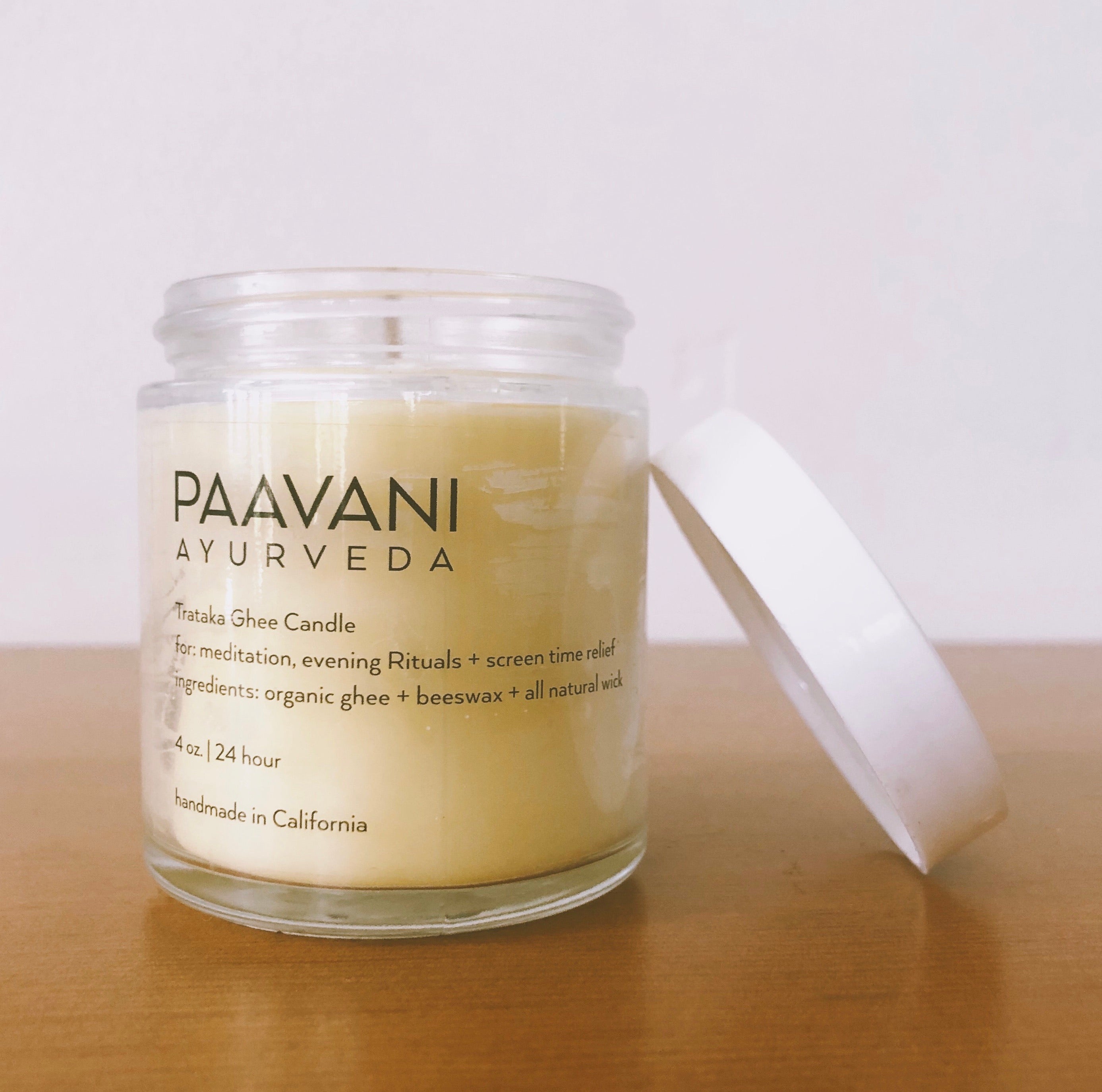 The Trataka Ghee Candle, encased in a glass jar labeled "PAAVANI," features a yellow balm crafted with turmeric, coconut wax, and essential oils. Inspired by Trataka practices, its soothing ingredients are designed to potentially enhance eye health.