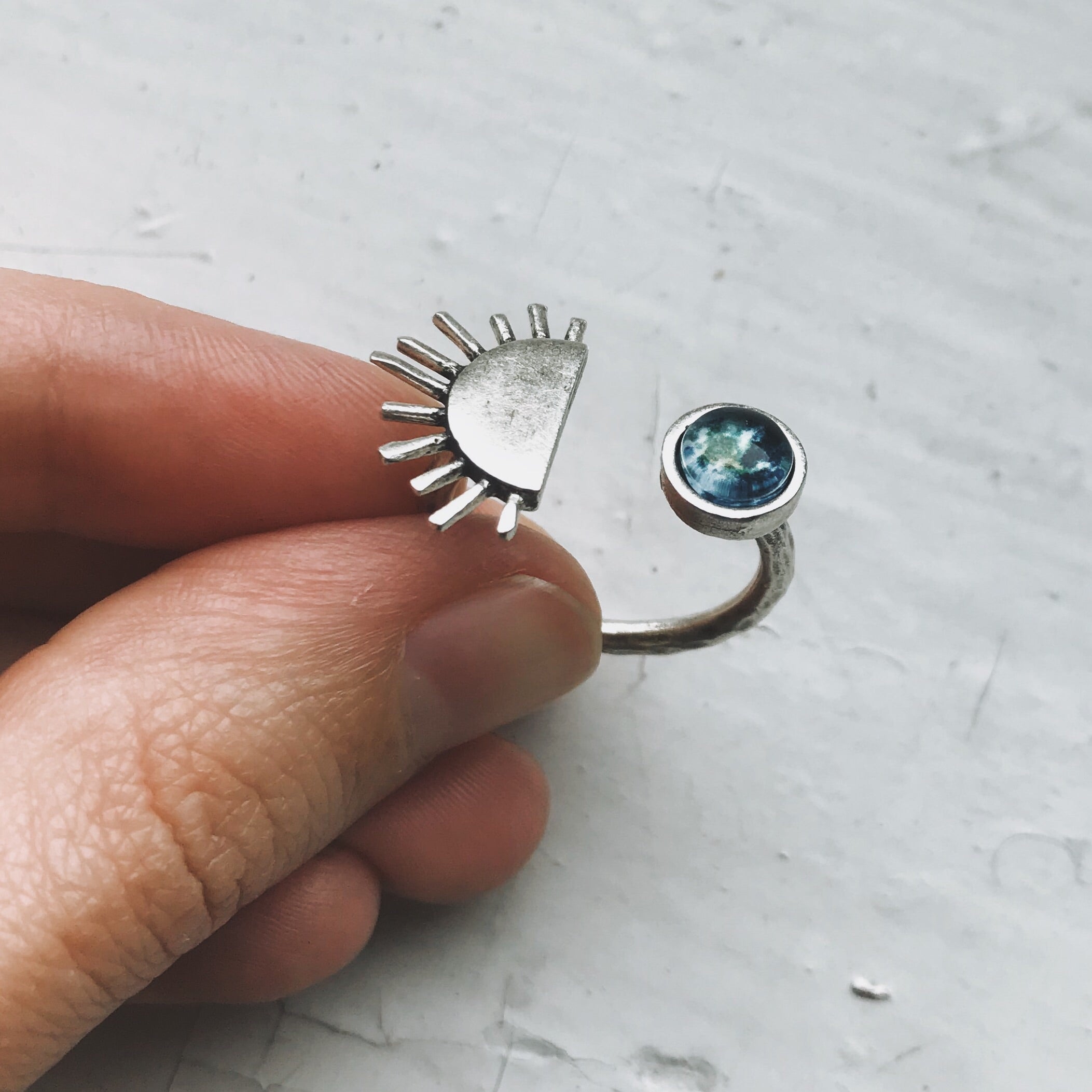 A hand showcases two exquisite pieces of Sunrise jewelry: a gold statement ring featuring a sun design and another adorned with a small globe image, both capturing the essence of elegance and adventure.