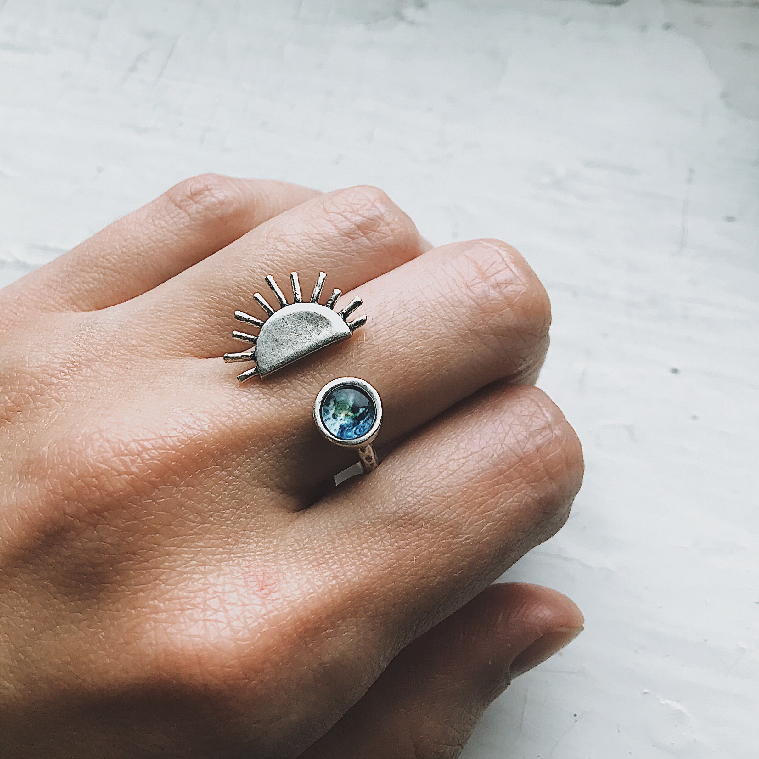 A hand showcases two exquisite pieces of Sunrise jewelry: a gold statement ring featuring a sun design and another adorned with a small globe image, both capturing the essence of elegance and adventure.