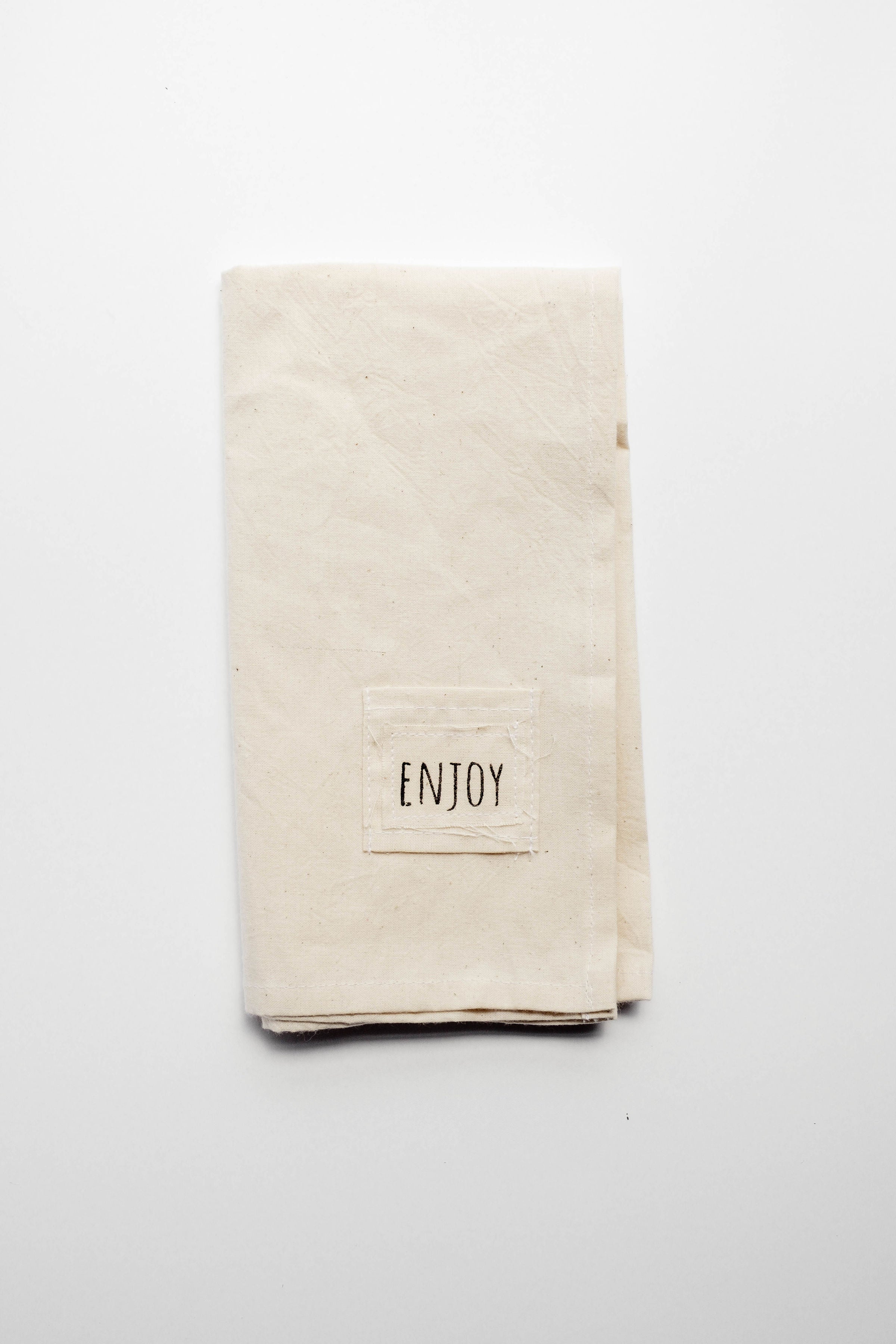 Pocket napkin set of four, skillfully crafted from up-cycled fabric, folded with a eucalyptus sprig and wooden ring, labeled "SAVOR.