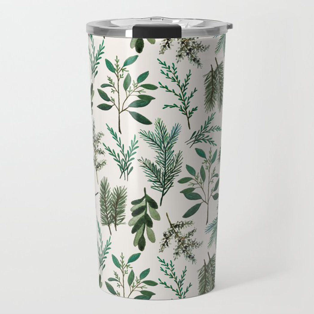 The Winter Branch Travel Mug, featuring a green botanical pattern and double-wall vacuum insulation, rests on a wooden surface with a blurred background.