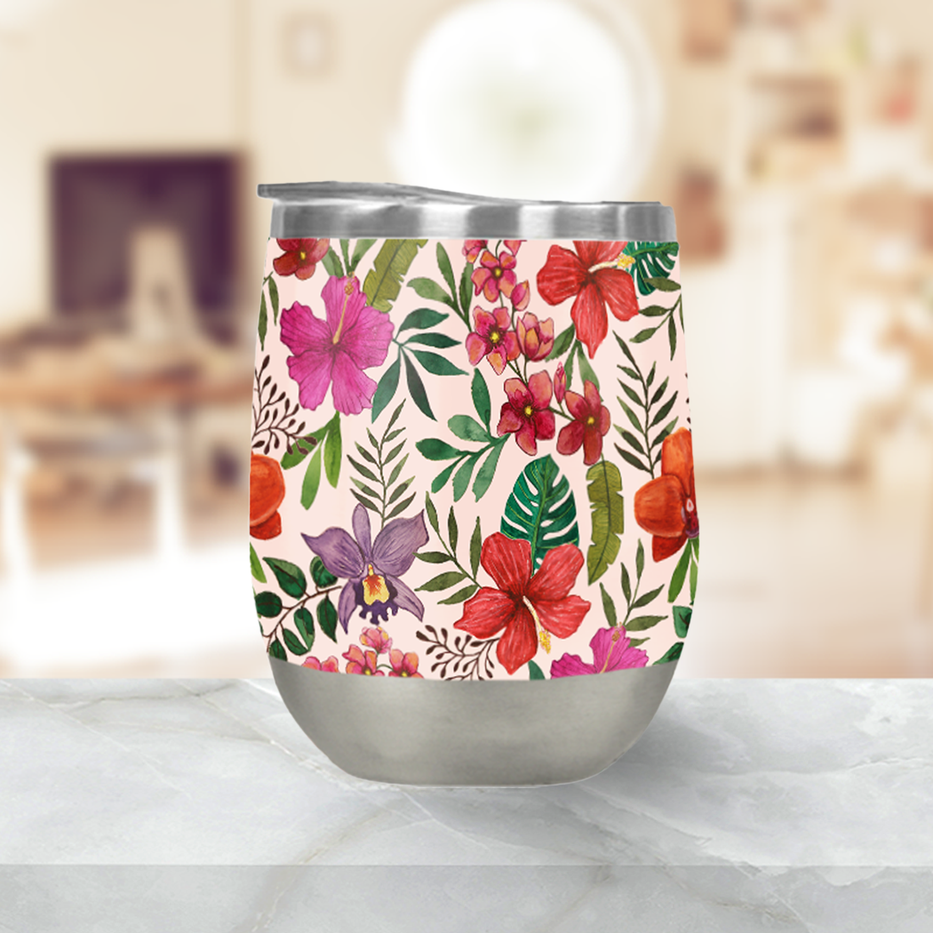 The Pink Tropical Flower Stemless Wine Tumbler features a stainless steel construction with double-wall insulation, adorned with red, pink, and purple floral motifs and green leaves set against a marble surface with a blurred background.