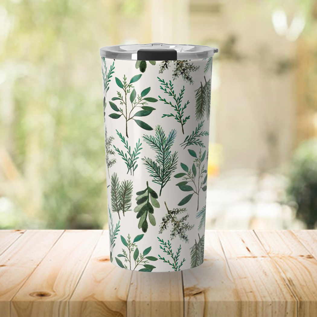 The Winter Branch Travel Mug, featuring a green botanical pattern and double-wall vacuum insulation, rests on a wooden surface with a blurred background.