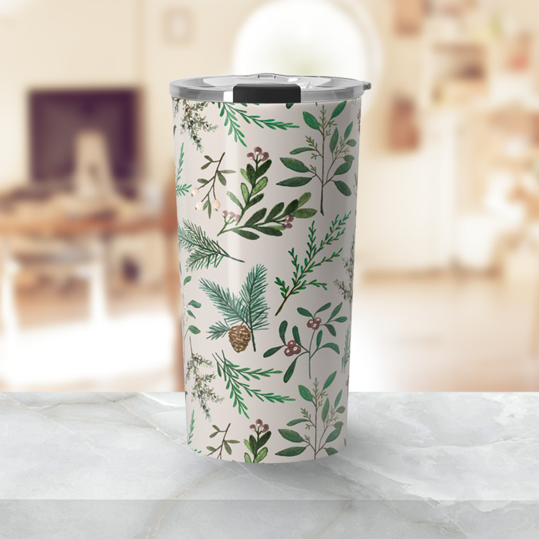 Introducing the Winter Berry Travel Mug: a tall, double-walled tumbler with a stainless steel interior. It showcases an elegant botanical leaf and pinecone design on a light backdrop. Resting serenely on a marble surface, it effortlessly blends into the blurred coziness of its surroundings. Ideal for travel mug enthusiasts who value both style and functionality.