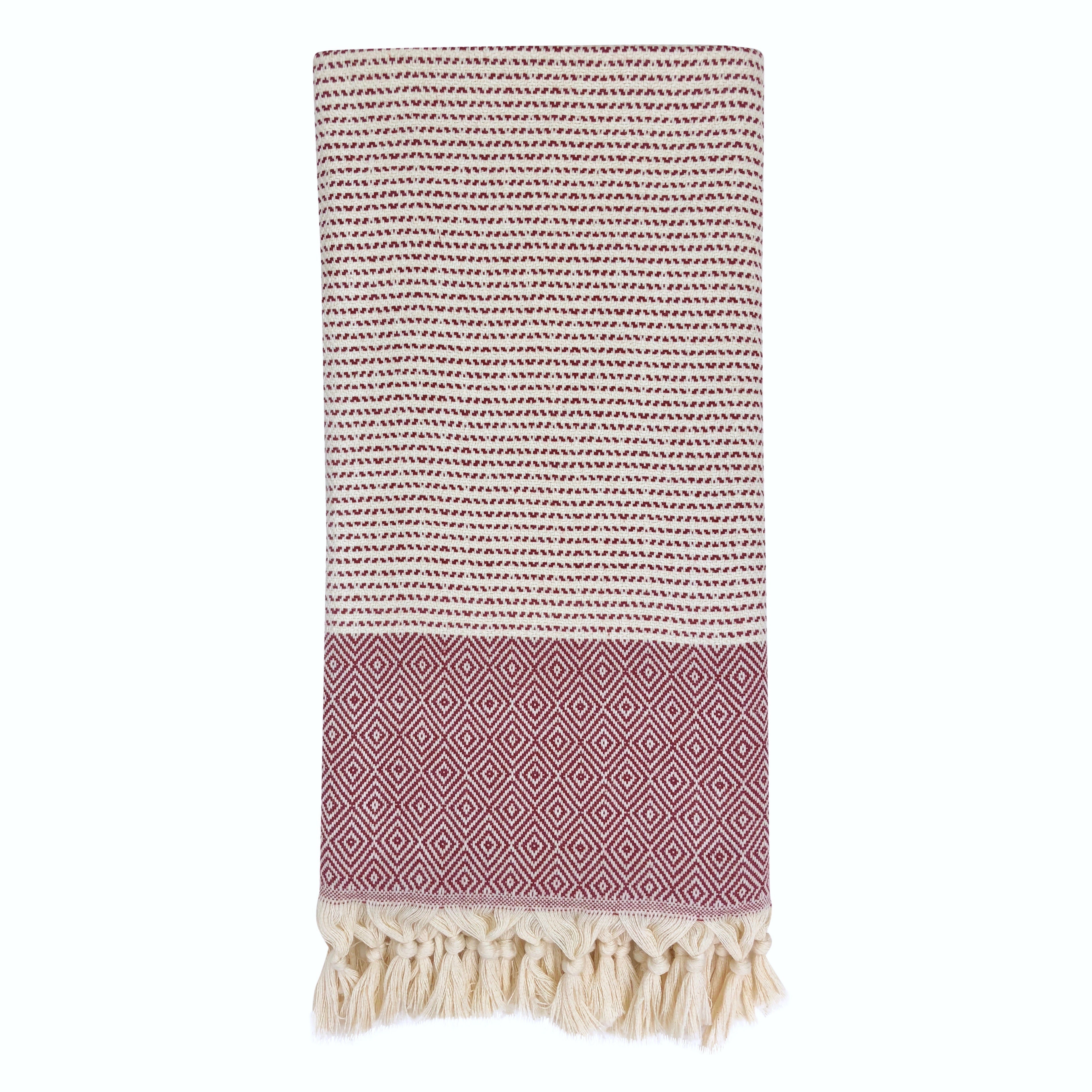 The Diamond Stripe Turkish Towel is crafted from luxurious Turkish cotton and features a folded, patterned design with a black and white striped top section and a red geometric-patterned bottom, complete with tasseled fringe at one end. It's perfect for adding elegance to beach outings or home decor.