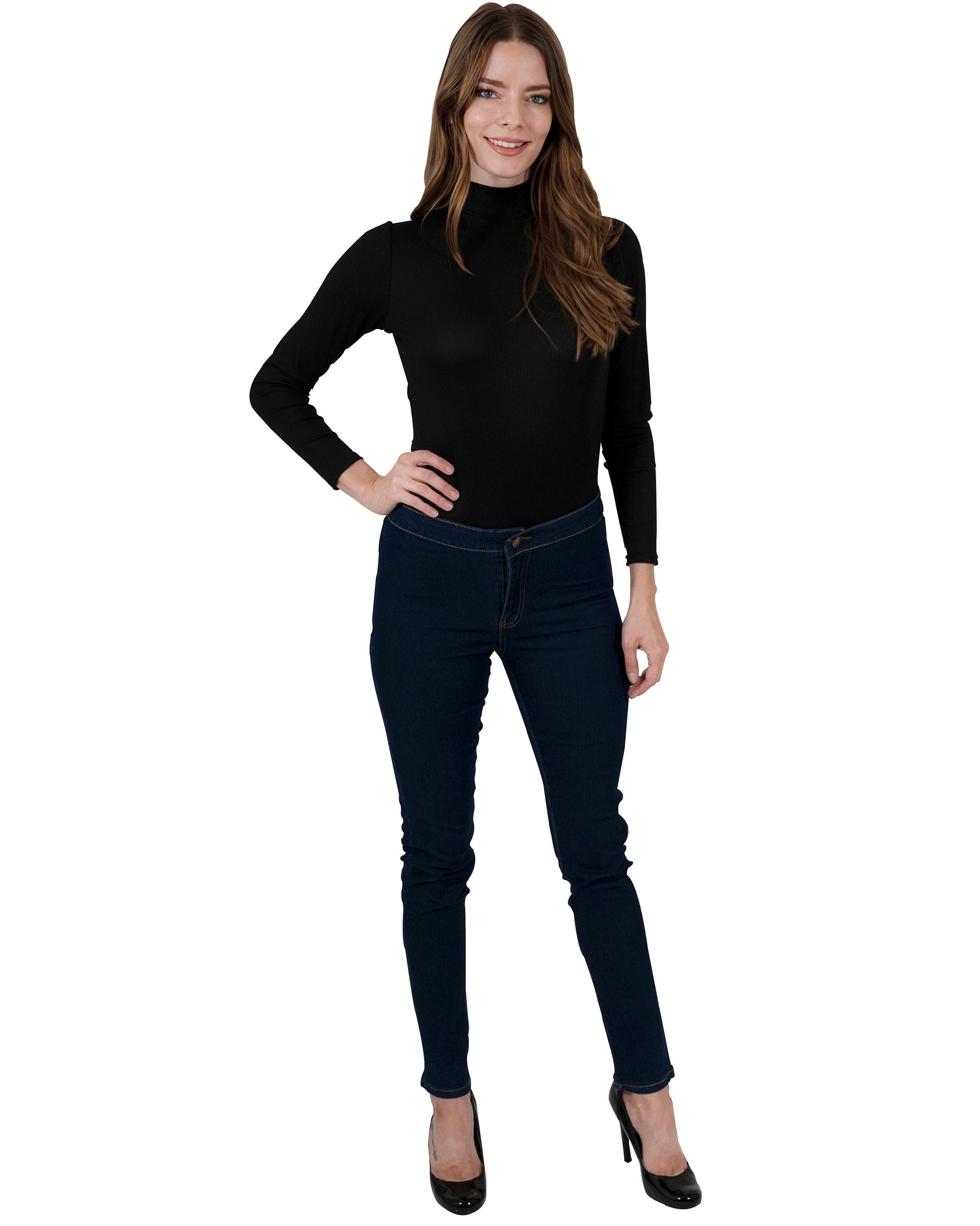 A woman in a black turtleneck and navy Walden Skinny Jeans stands with one hand on her hip, smiling.