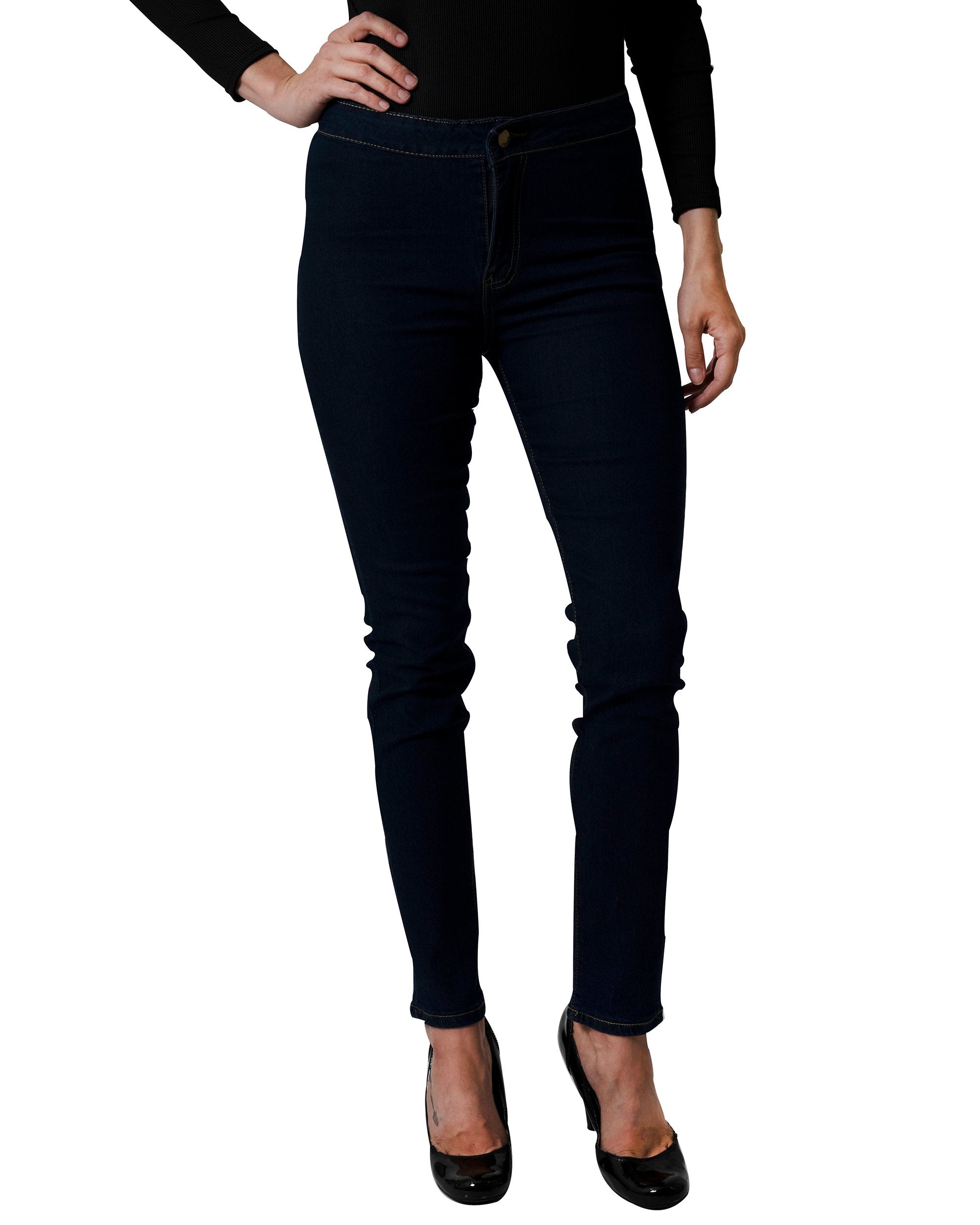 A woman in a black turtleneck and navy Walden Skinny Jeans stands with one hand on her hip, smiling.