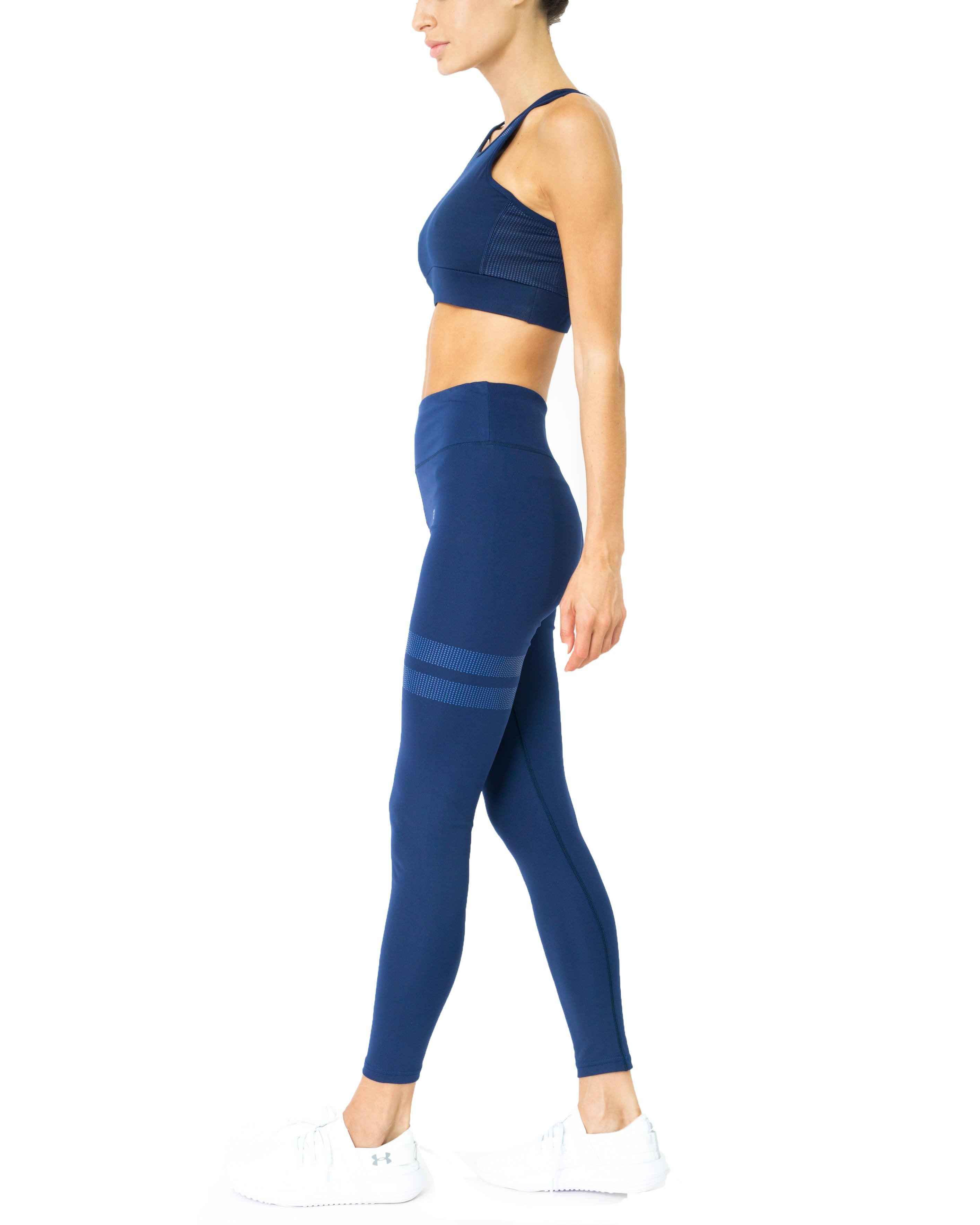 A person in the navy blue Ashton Set, featuring a compression sports bra and tummy-control leggings, walks in profile against a white background.