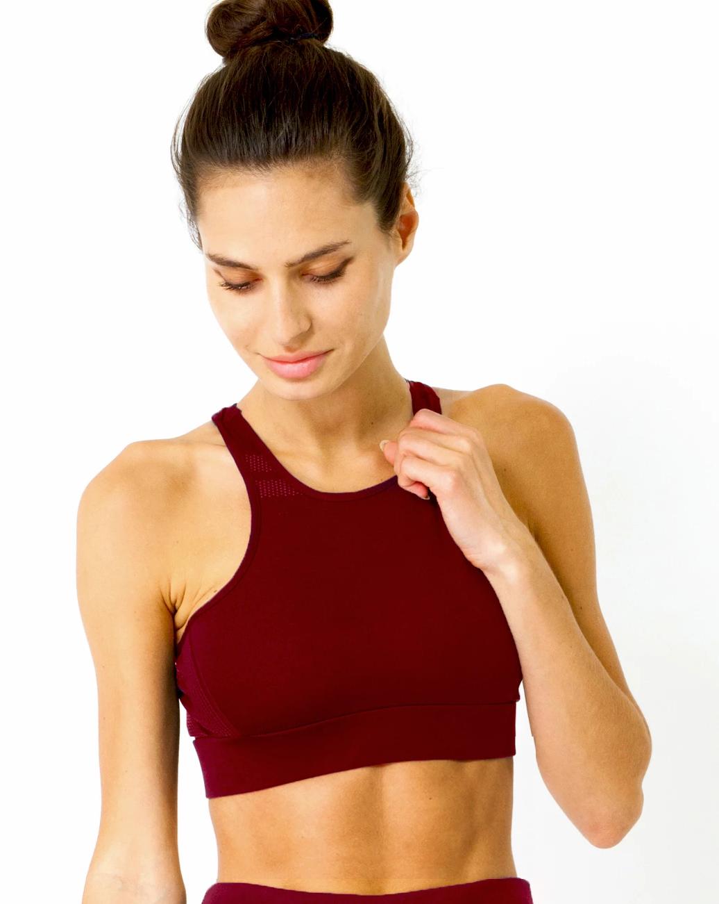 A person with hair in a bun is looking down while wearing the Ashton Sports Bra in maroon against a white background.