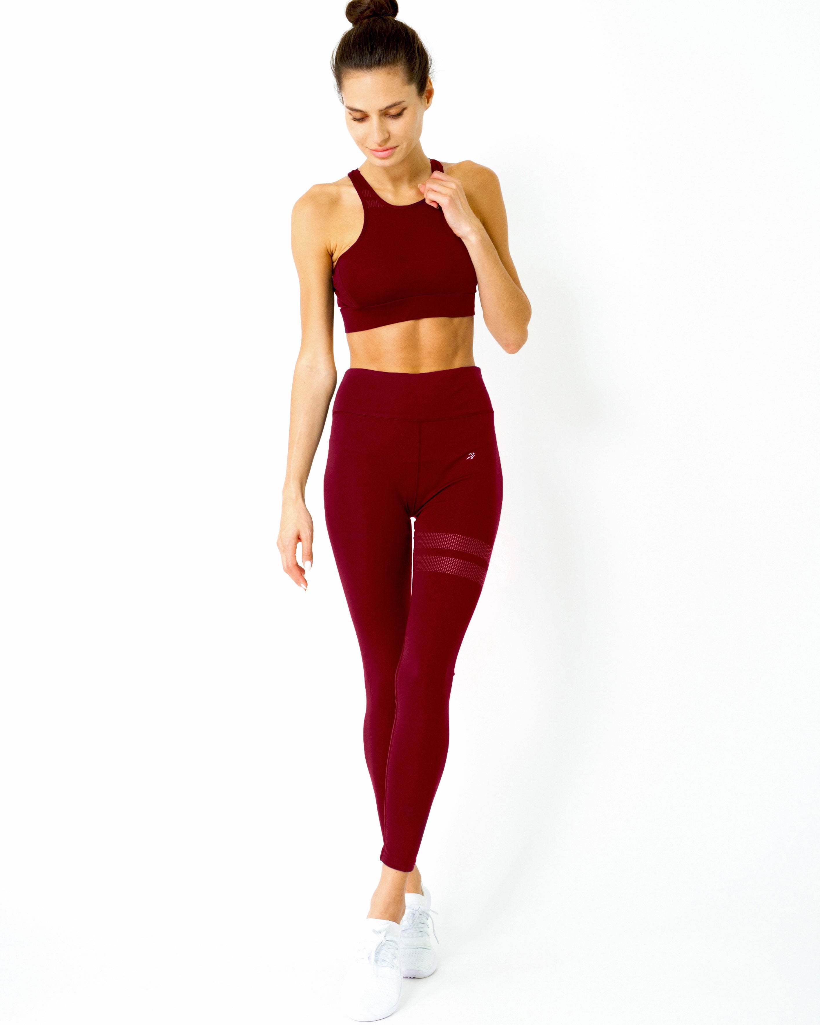 A person with hair in a bun is looking down while wearing the Ashton Sports Bra in maroon against a white background.