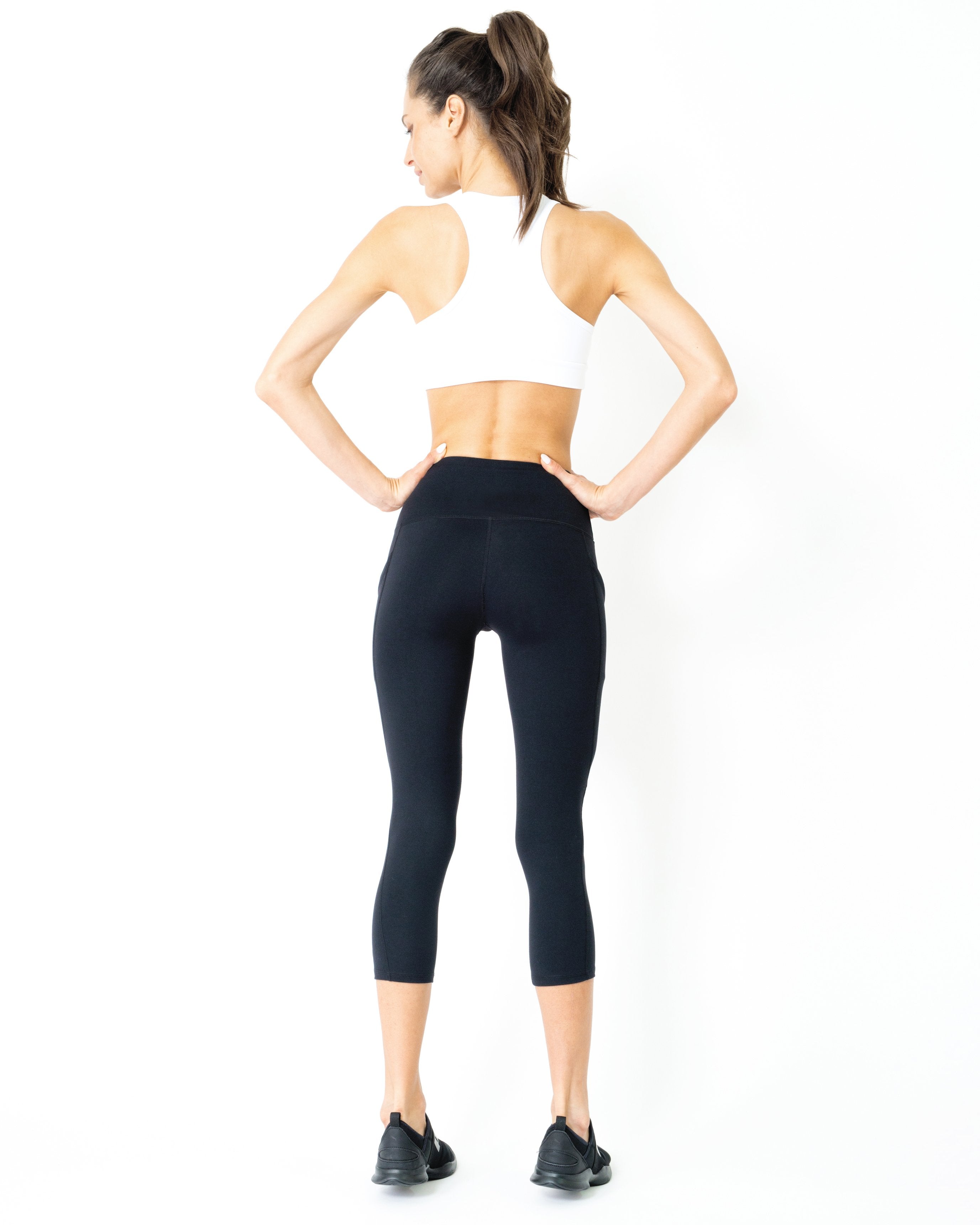 A person wearing Jolie High-Waisted Capri Leggings with hip pockets stands barefoot against a plain white background, hands in the side pockets.