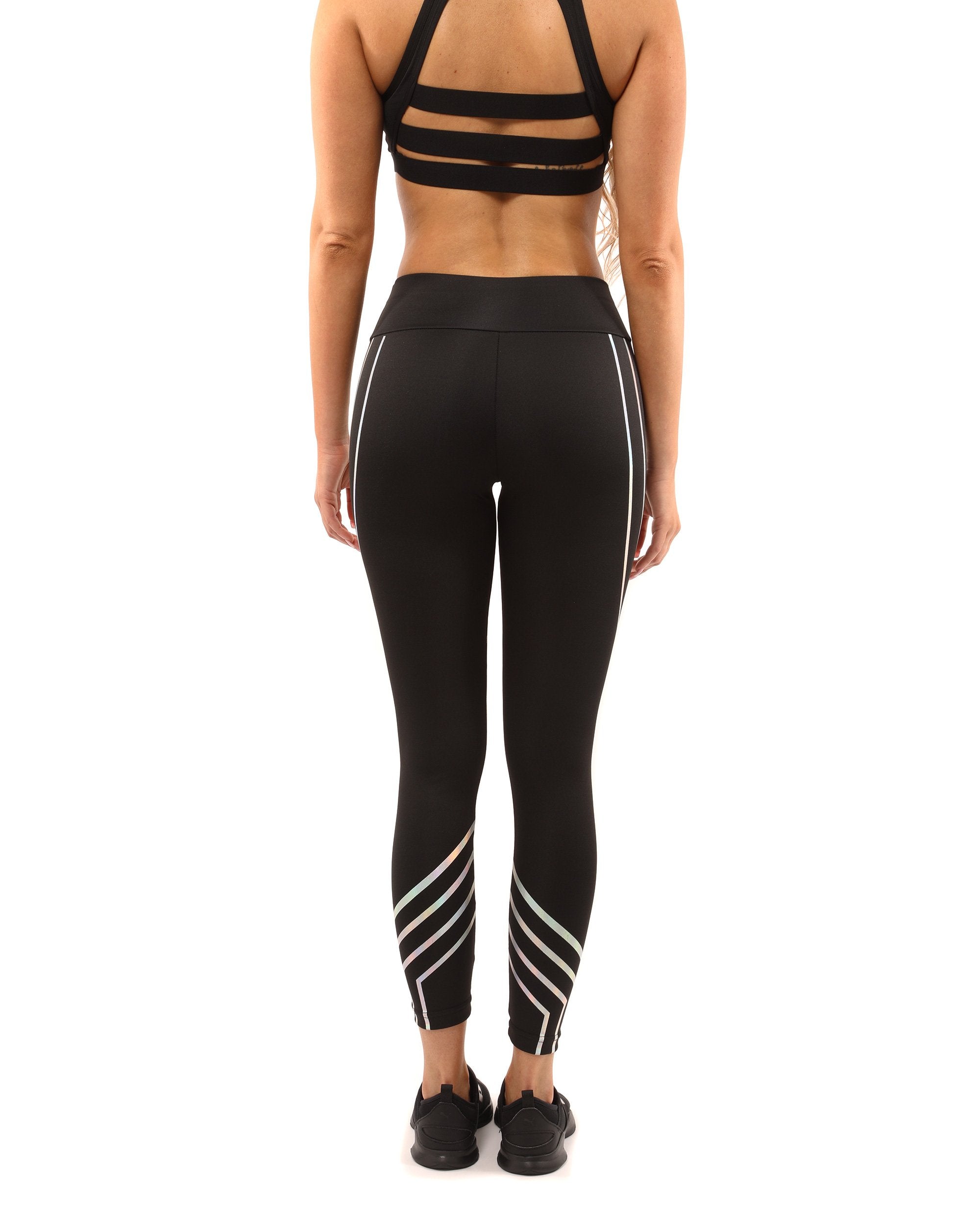 A person wearing the Laguna Leggings in black, featuring curved reflective stripes, along with a matching sports bra, stands confidently against a plain background, highlighting the sculpted compression fit.