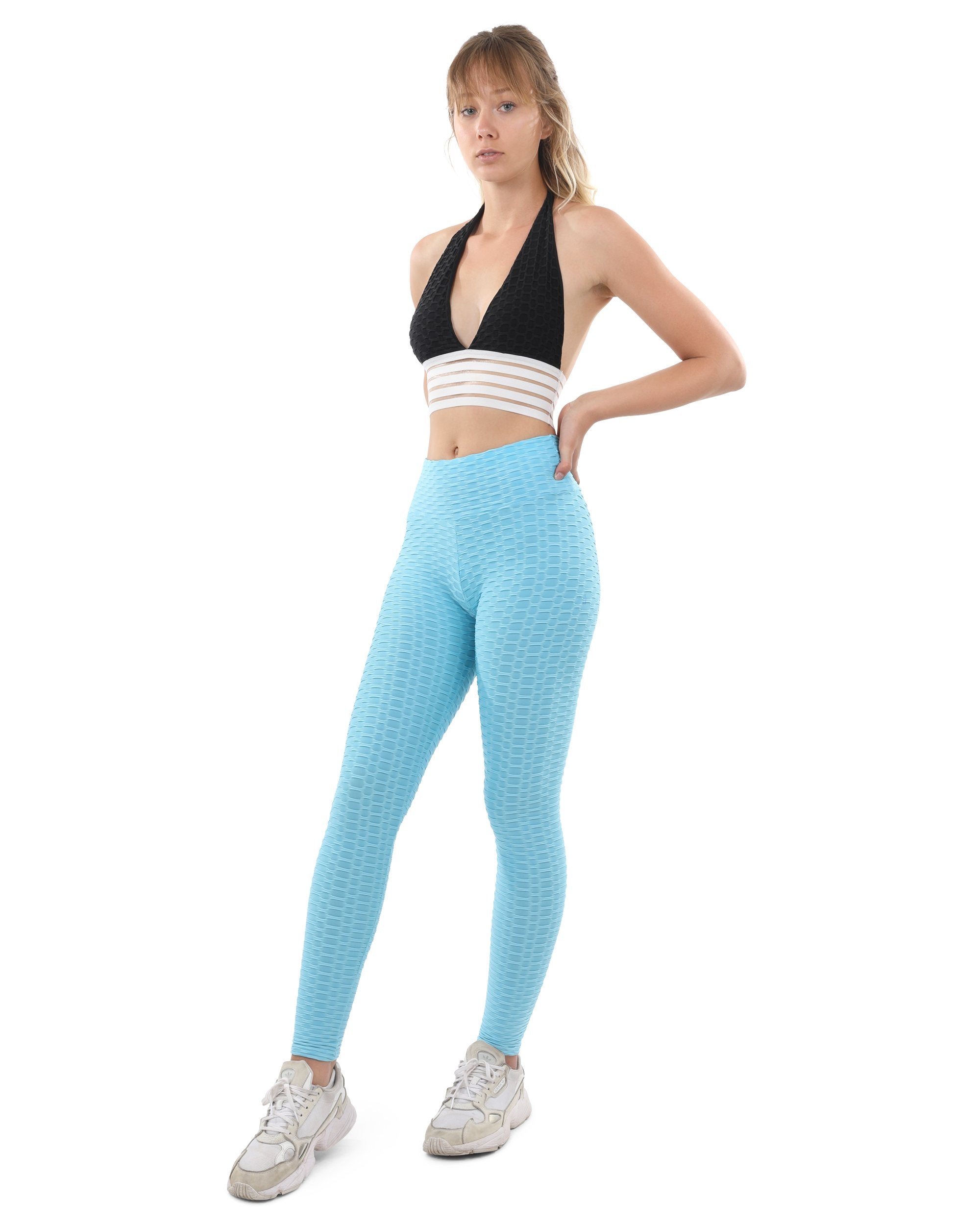 A person wearing Aqua Bentley Leggings, which feature a textured finish, stands against a plain background, paired with a striped crop top and white sneakers. These high-waisted leggings provide flattering slimming support suitable for any occasion.