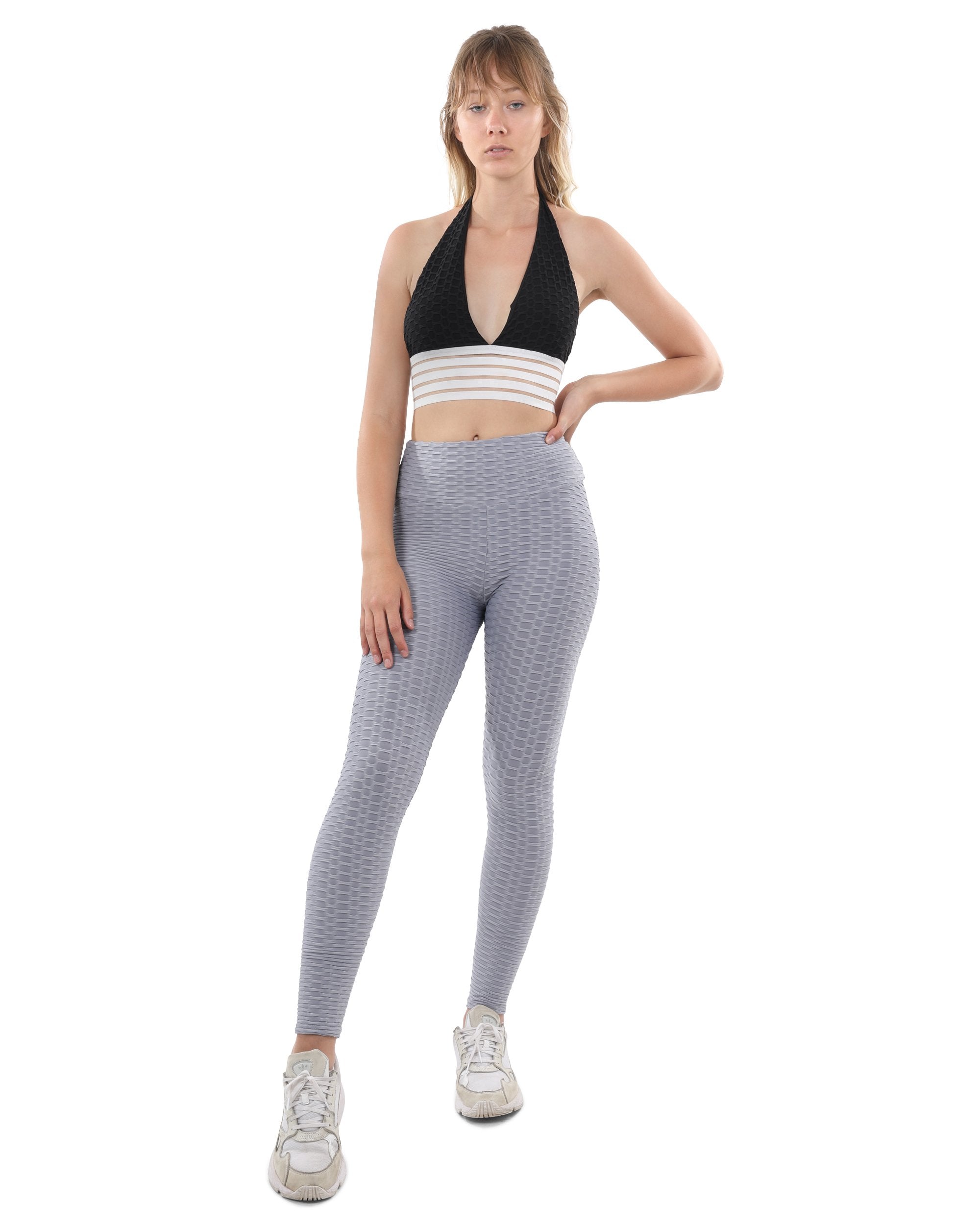 A person wearing a white and gray striped crop top with Bentley Leggings in grey, standing with hands on hips, and finishing the look with slimming white sneakers.