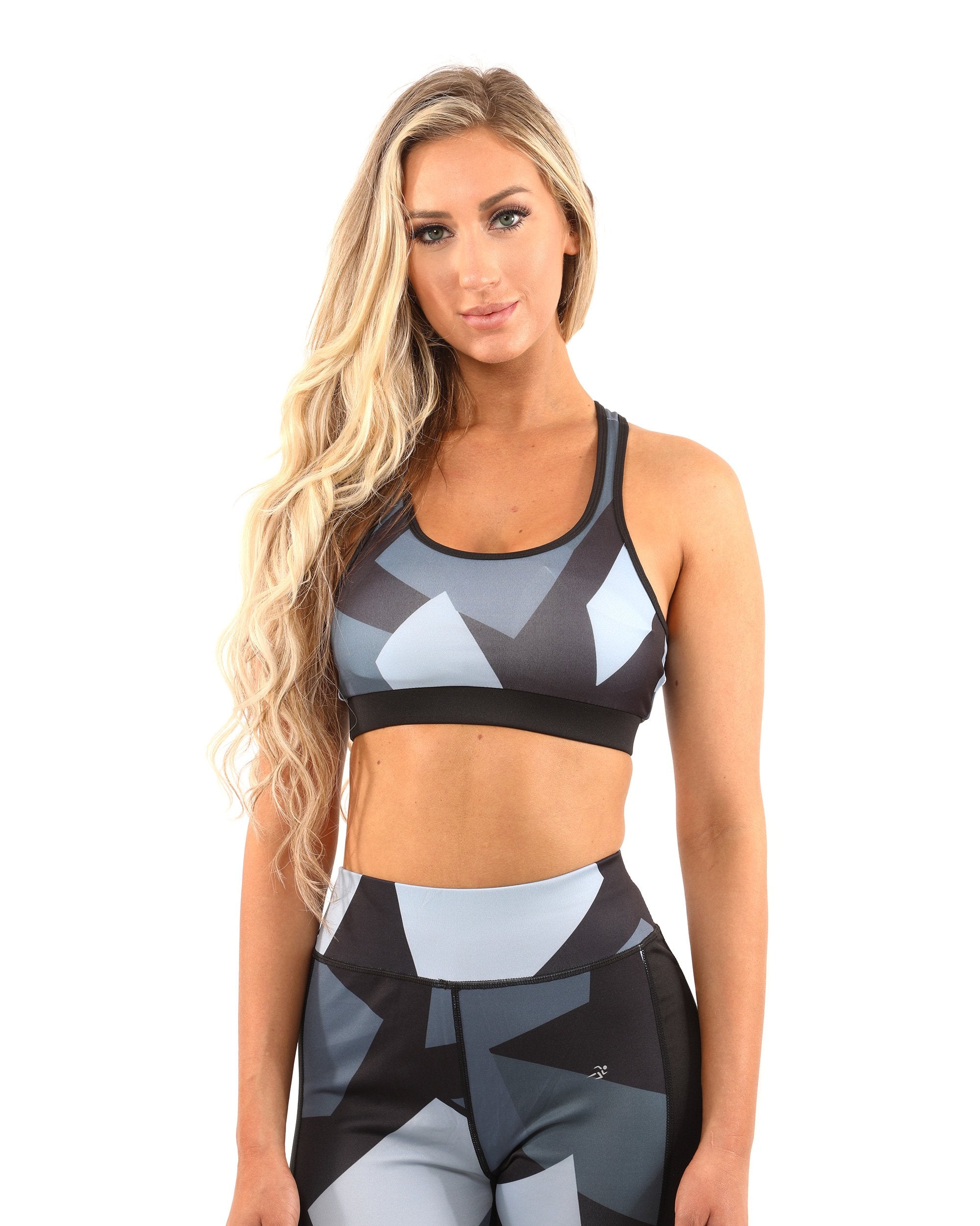 A person with long blonde hair is wearing the Bondi Sports Bra - Black/Grey, featuring a geometric-patterned compression fit and racerback design, accompanied by matching leggings, standing against a white background.