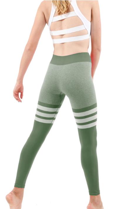 A person is wearing the Cassidy Legging - Green, which features high-waisted, green and gray fabric with white stripes around the thighs, while standing on a white background.