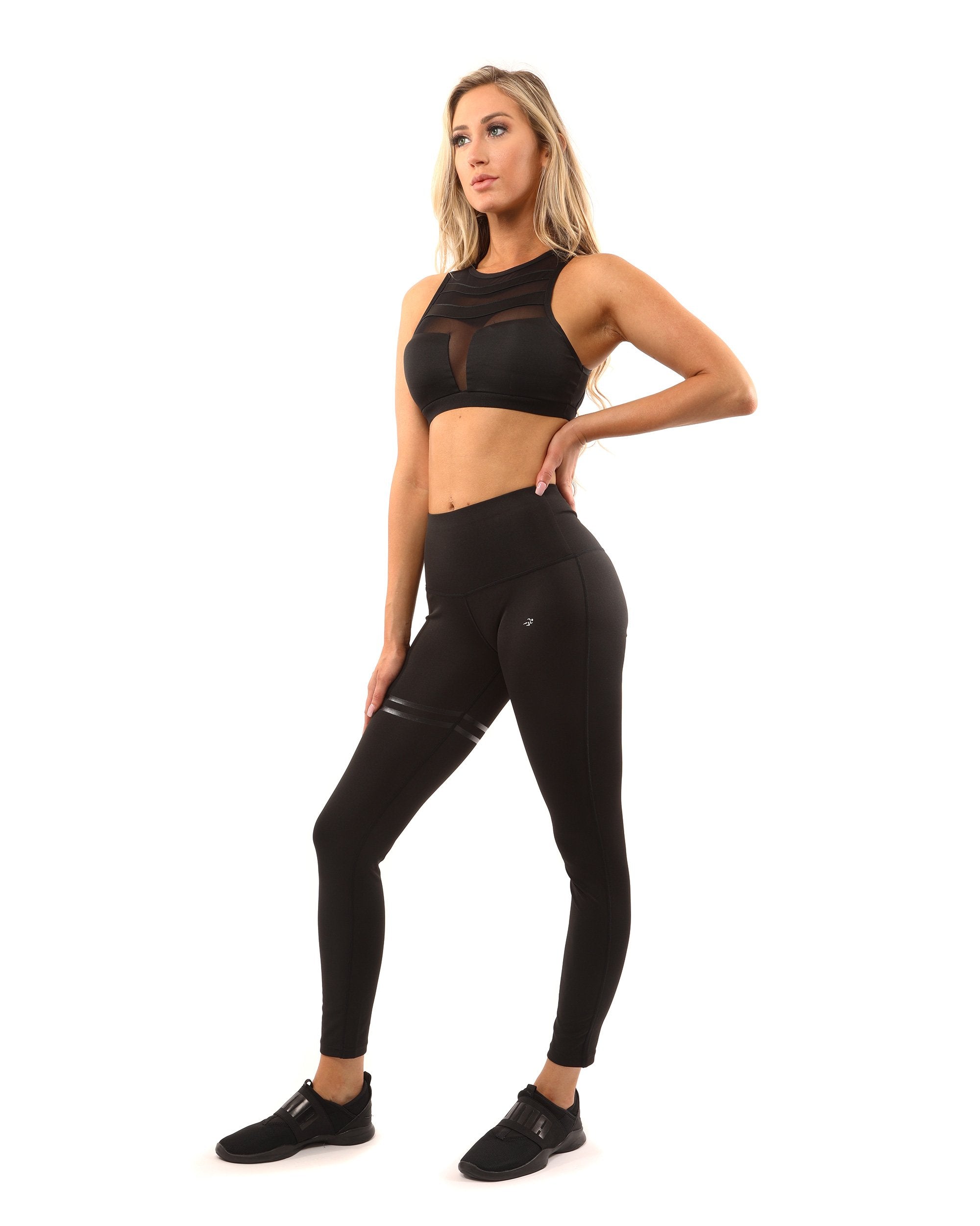 A person wearing the Laguna Sports Bra in black, featuring mesh detailing and a racerback design, stands against a white background.