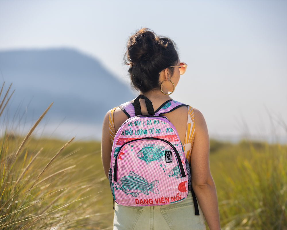 Introducing the Scout Backpack: a vividly designed accessory featuring a yellow front, an orange top, and blue patterned sides. Crafted from upcycled materials, it includes padded shoulder straps for comfort. The logo elegantly embellishes the front pocket, adding a stylish flair.