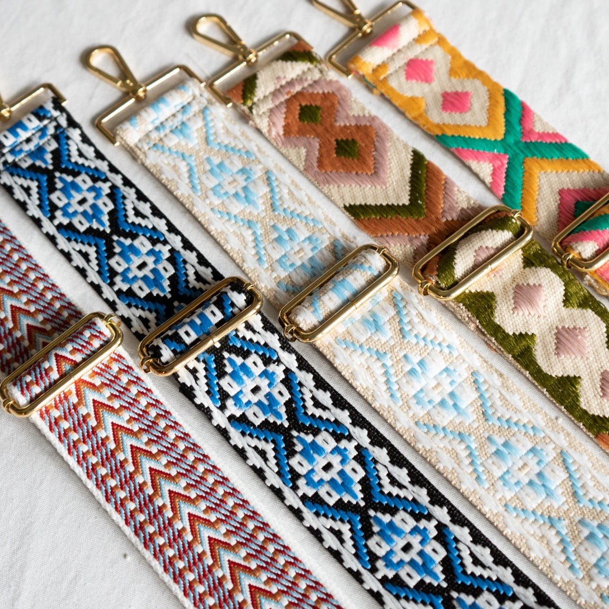 A selection of six vibrant and colorful straps from our "Bag Straps | 30 Styles" collection, featuring gold hardware against a white backdrop, showcases an array of geometric patterns in lively hues such as blue, red, green, and pink.