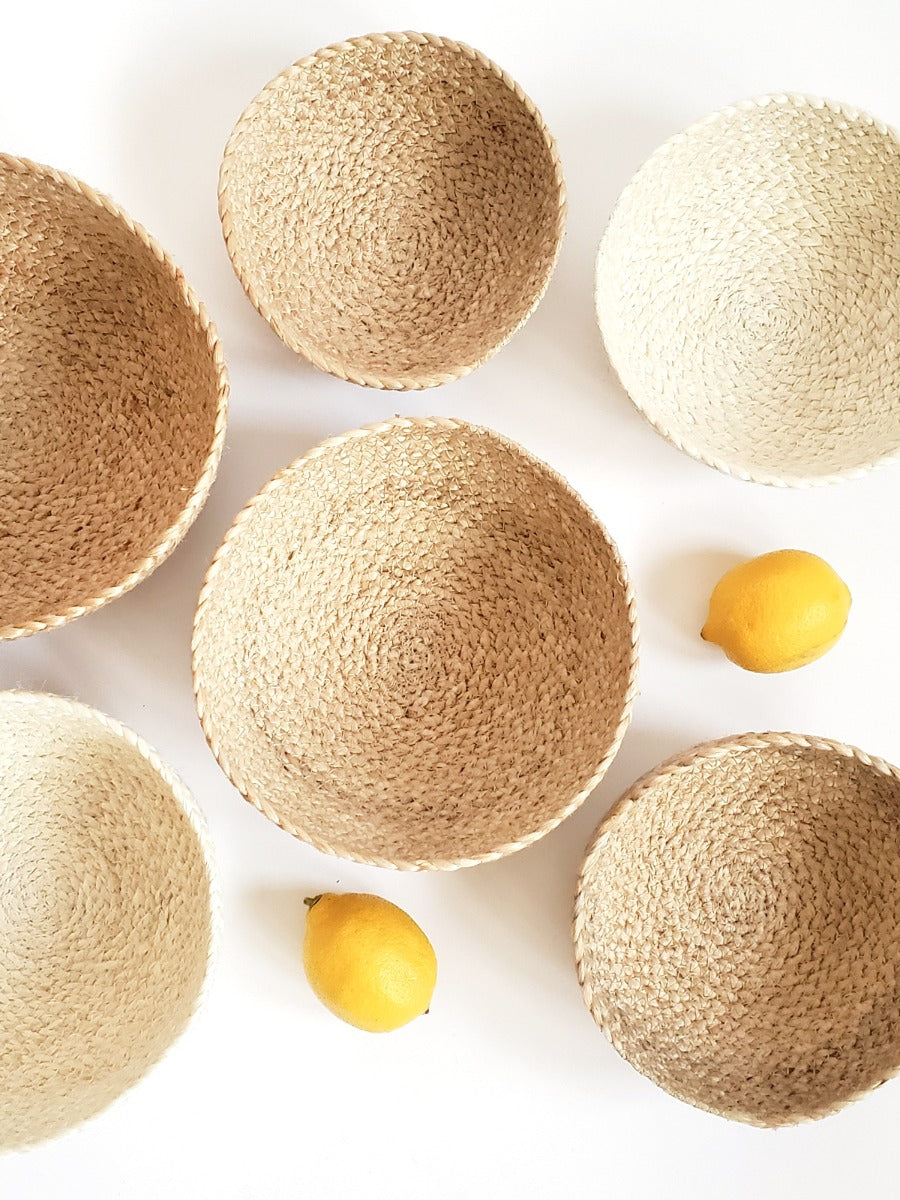 On a flat surface against a plain background, a set of four Kata Candy Bowls in white, crafted by fair trade artisans, is displayed. These versatile woven straw baskets highlight the beauty and authenticity of natural jute.