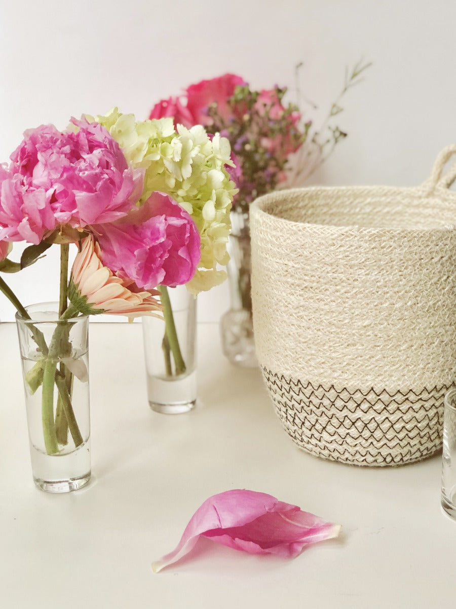 The Amari Loop Bin - Black, a beige and black woven basket featuring a loop handle, is elegantly displayed on a plain white background. Sustainably handmade by Fair Trade artisans, it seamlessly blends style with ethical craftsmanship.