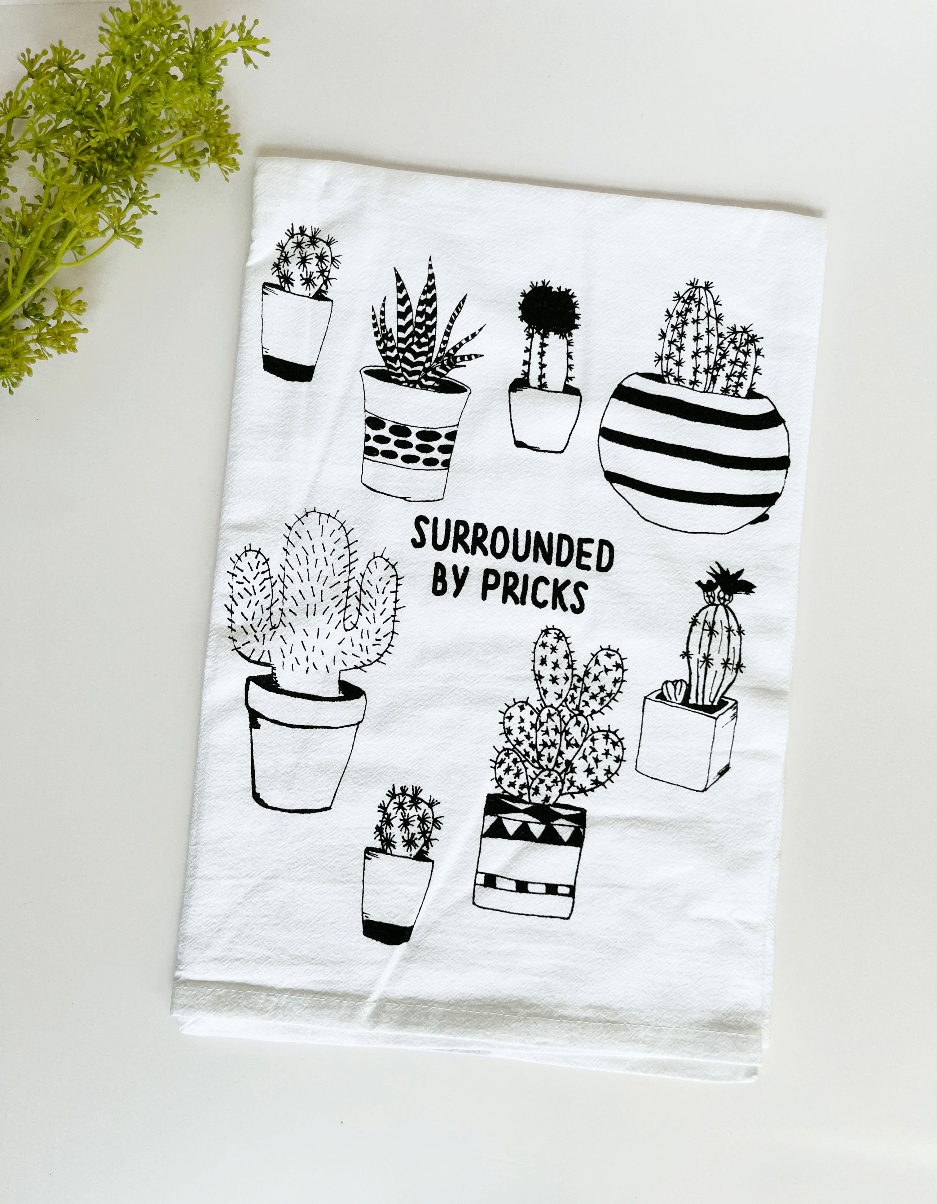 Introducing the "Surrounded by Pricks Cotton Kitchen Towel," a lint-free cotton towel featuring black line drawings of various potted cacti accompanied by the playful text "Surrounded by Pricks." Ideal for an eco-friendly kitchen, this towel makes a wonderful gift for plant enthusiasts who value humor and sustainability.