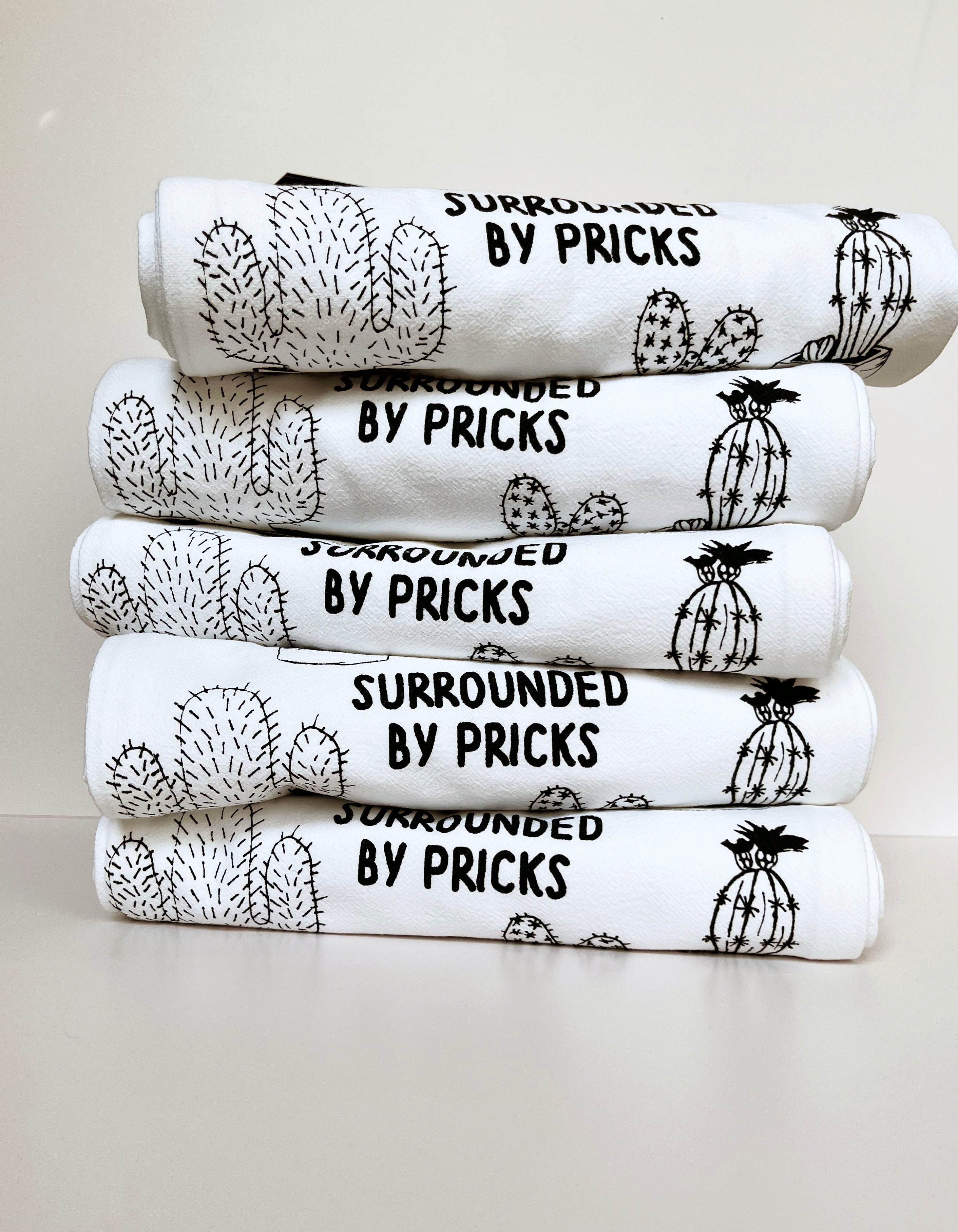 Introducing the "Surrounded by Pricks Cotton Kitchen Towel," a lint-free cotton towel featuring black line drawings of various potted cacti accompanied by the playful text "Surrounded by Pricks." Ideal for an eco-friendly kitchen, this towel makes a wonderful gift for plant enthusiasts who value humor and sustainability.