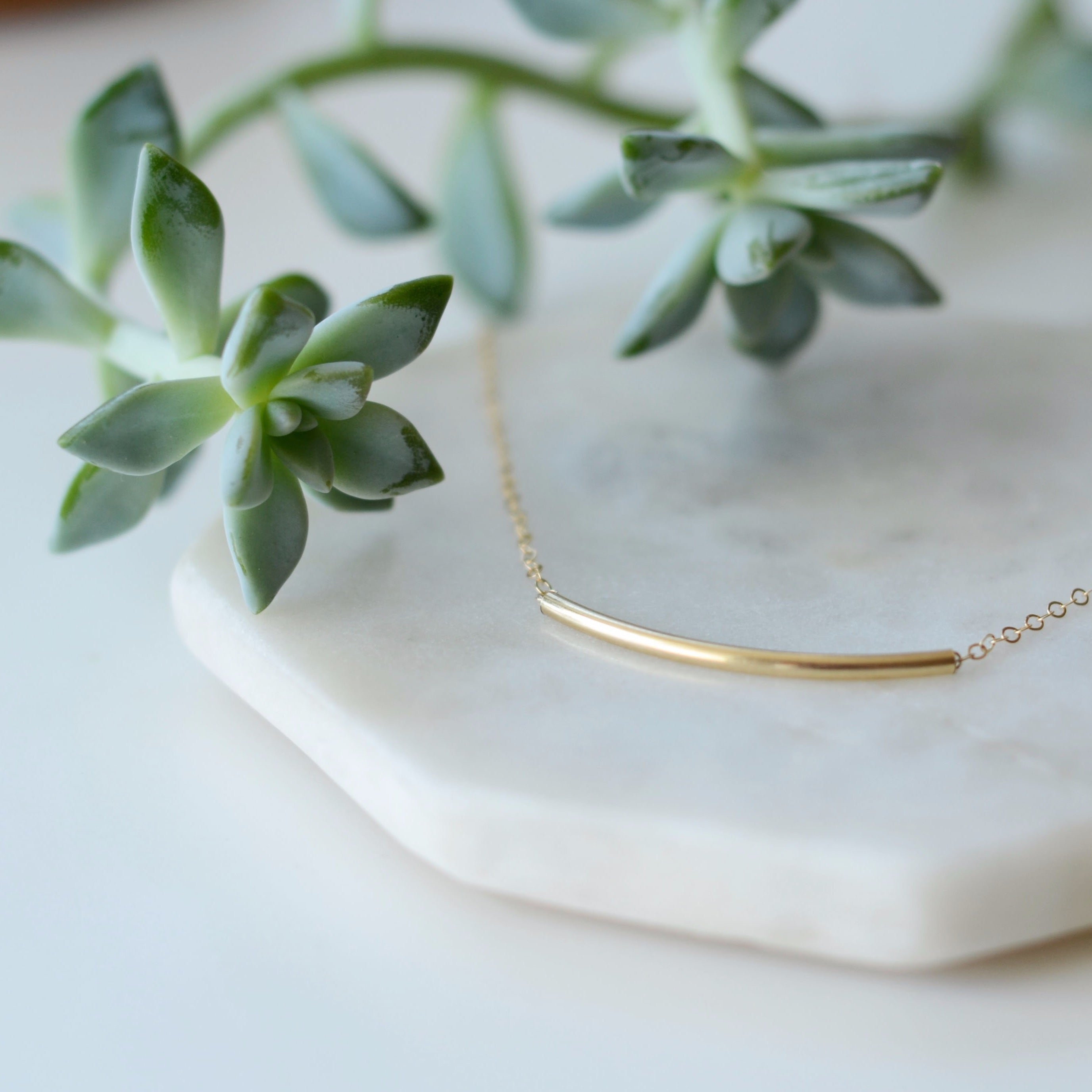 Amidst lush greenery, a person smiles outdoors, wearing a floral shirt and the delicate Talitha Necklace in 14k gold fill.