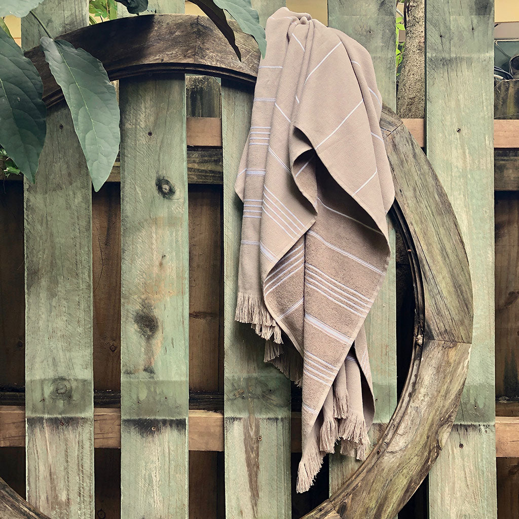 The Classic Terry Turkish Towel is a handmade white towel featuring horizontal gray stripes and fringed edges, ideal for enhancing the elegance of your bath collection.